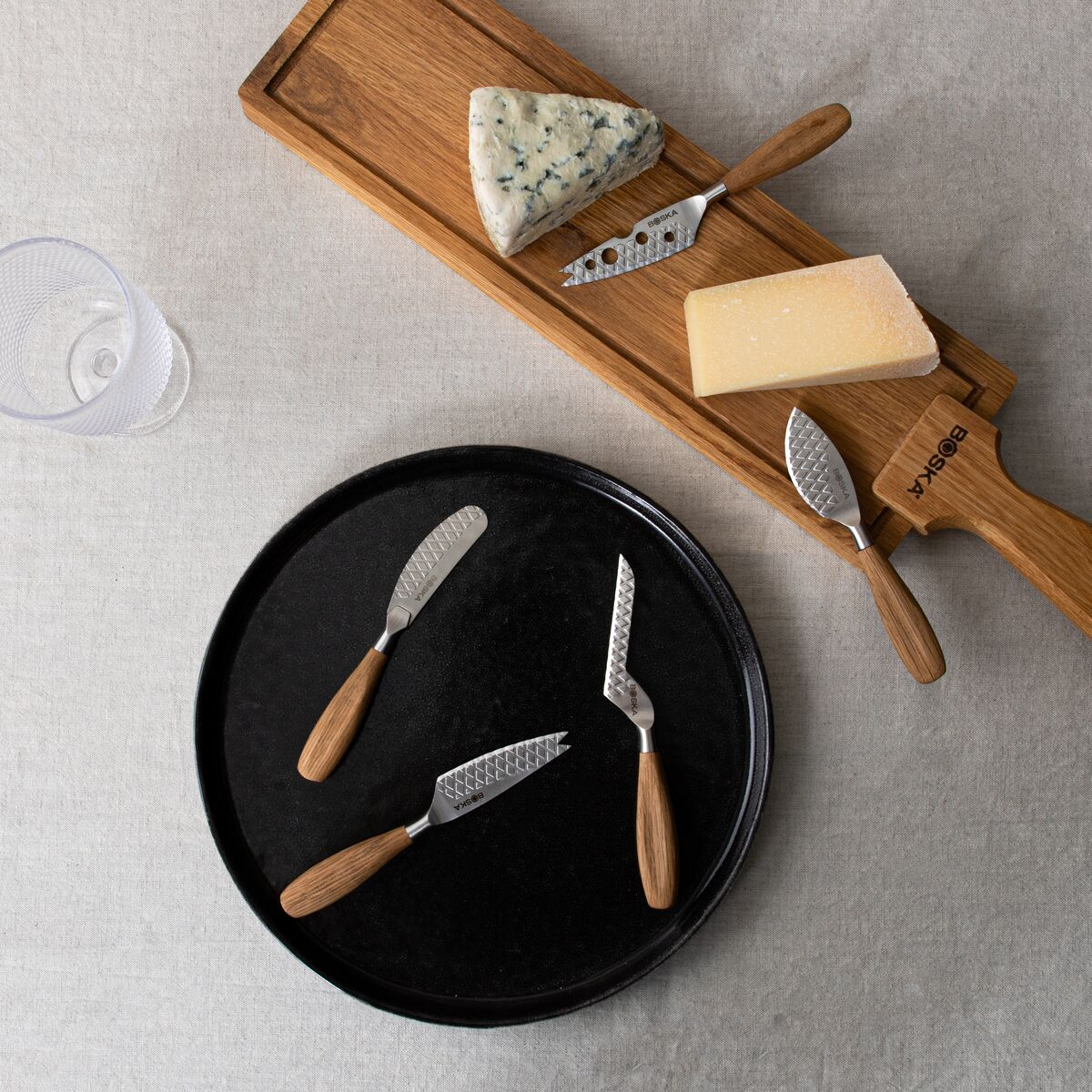 Cheese board with blue cheese, hard cheese, and three cheese knives on a black plate.