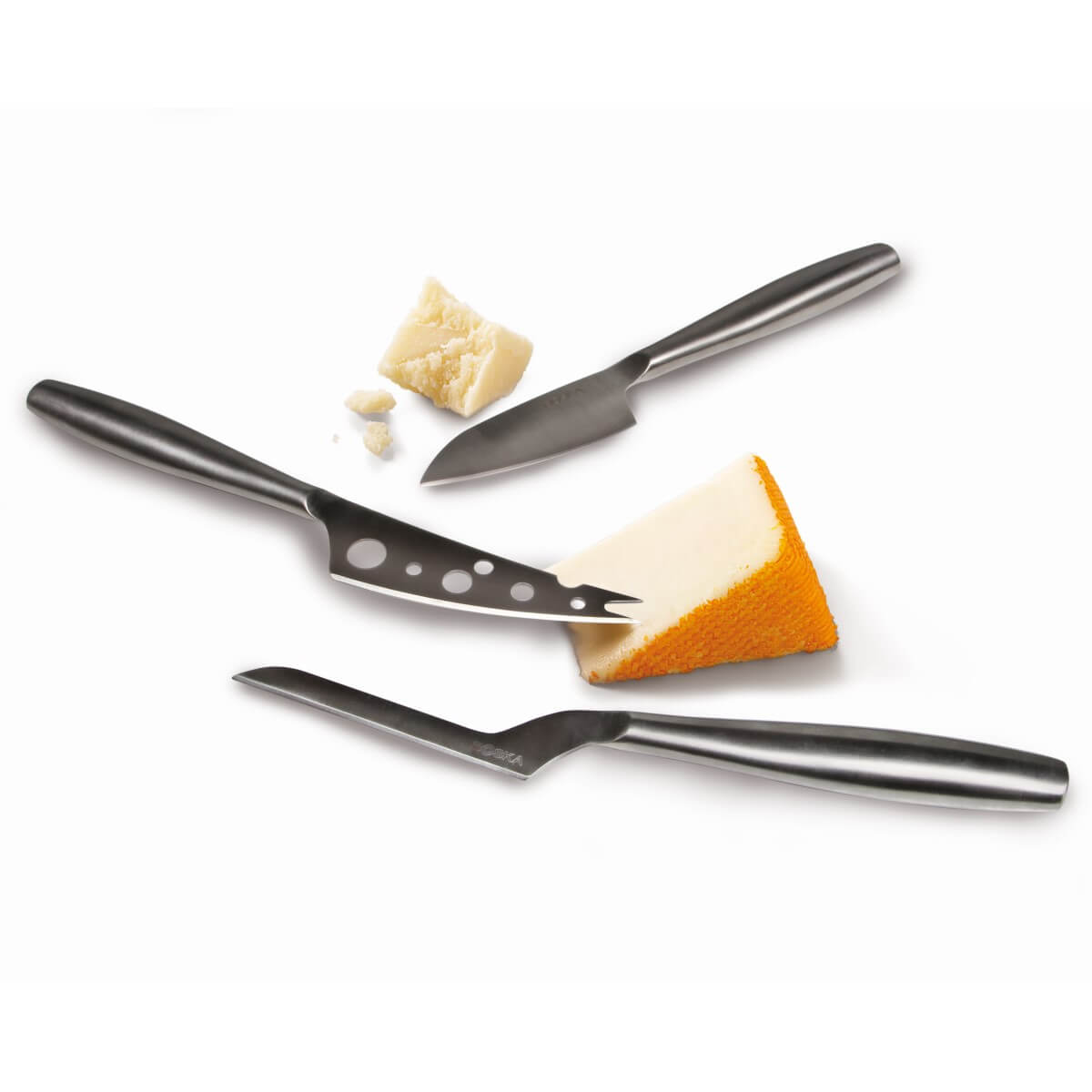 Three silver cheese knives are placed next to cheese on a white background.