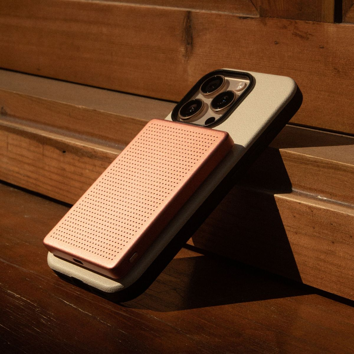 Un power bank color oro rosa è attaccato a una custodia per telefono beige chiaro.