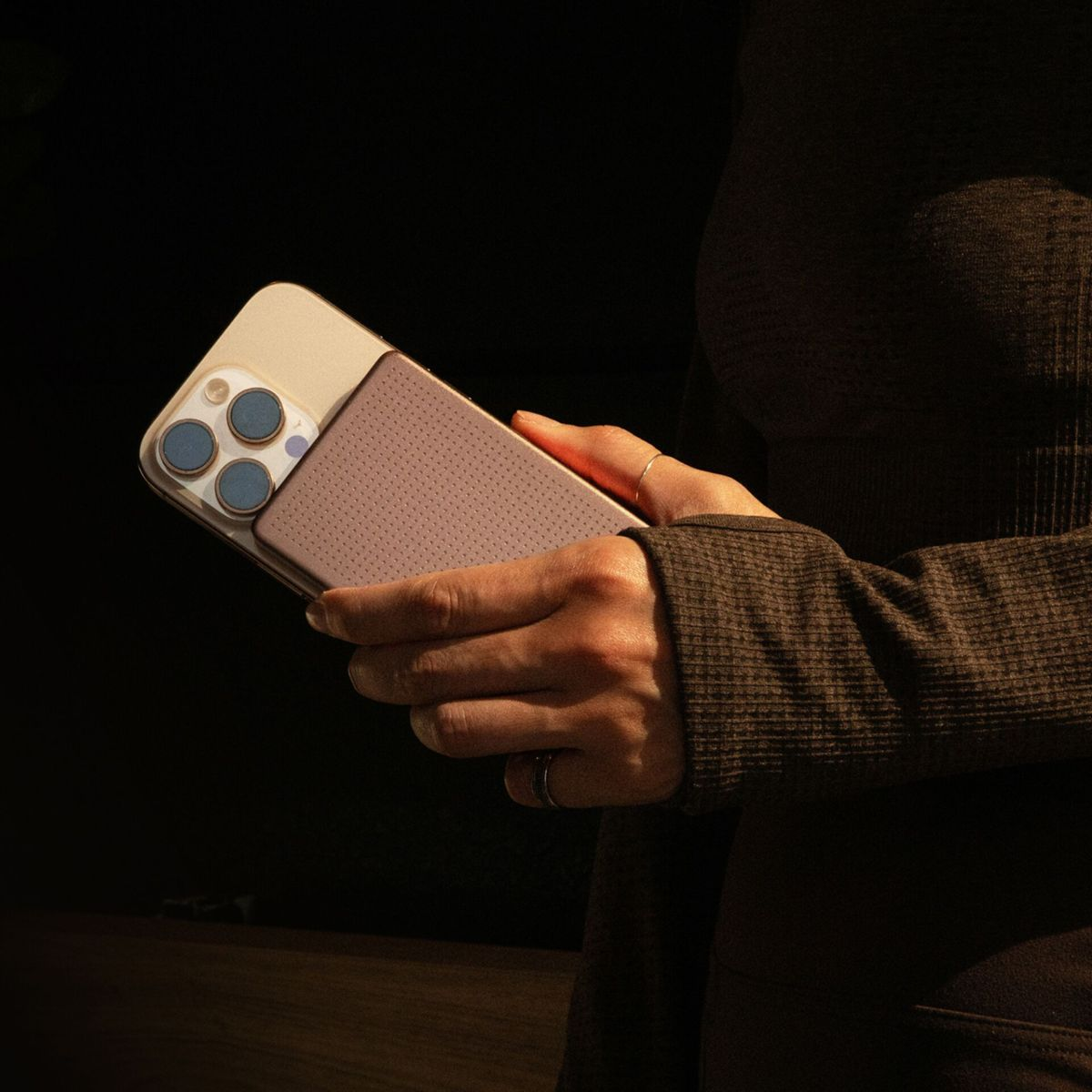 Una persona tiene un telefono con cover rosa puntinata e alloggiamento dorato.