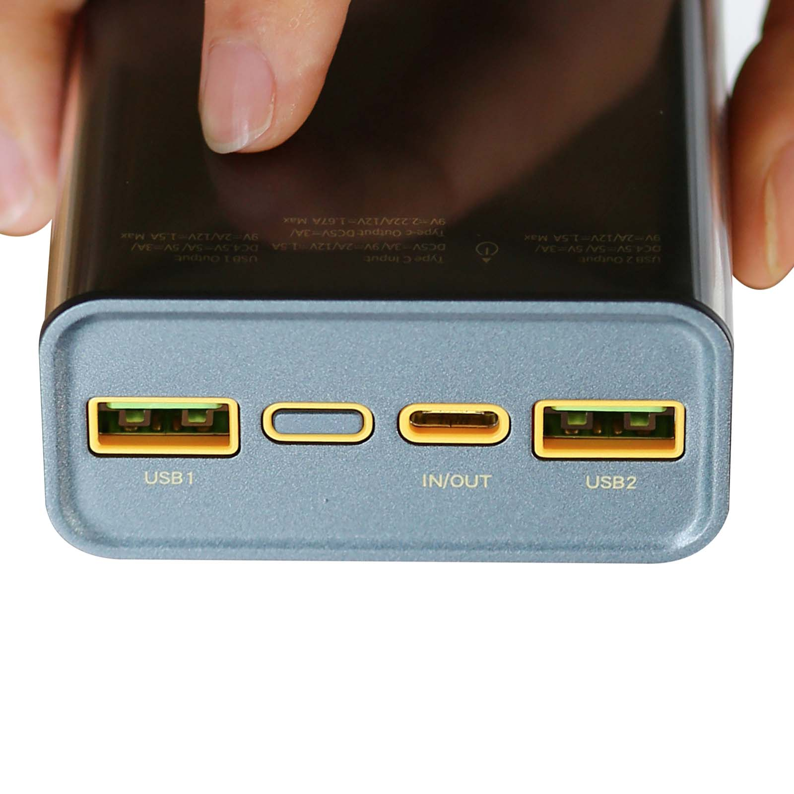 Un doigt touche le boîtier d'une batterie externe avec ports USB-A et USB-C.