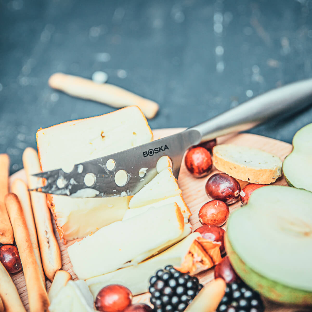 Cheese board with assorted cheeses, breadsticks, grapes, berries, and pear slices.