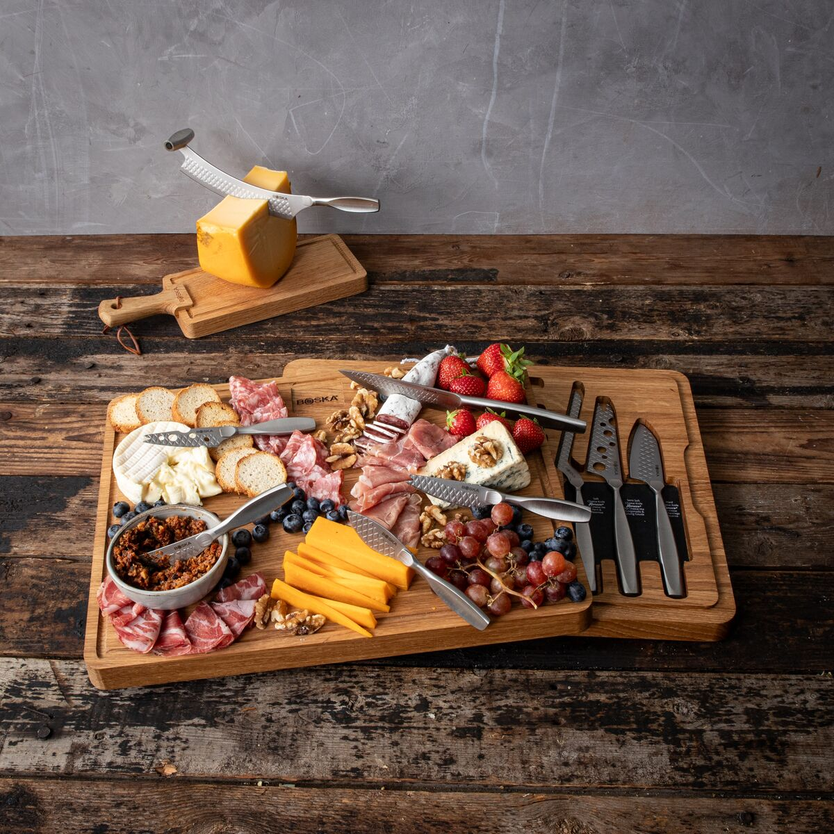 Cheese board with charcuterie, cheese, fruits, nuts, and crackers; cheese knives nearby.
