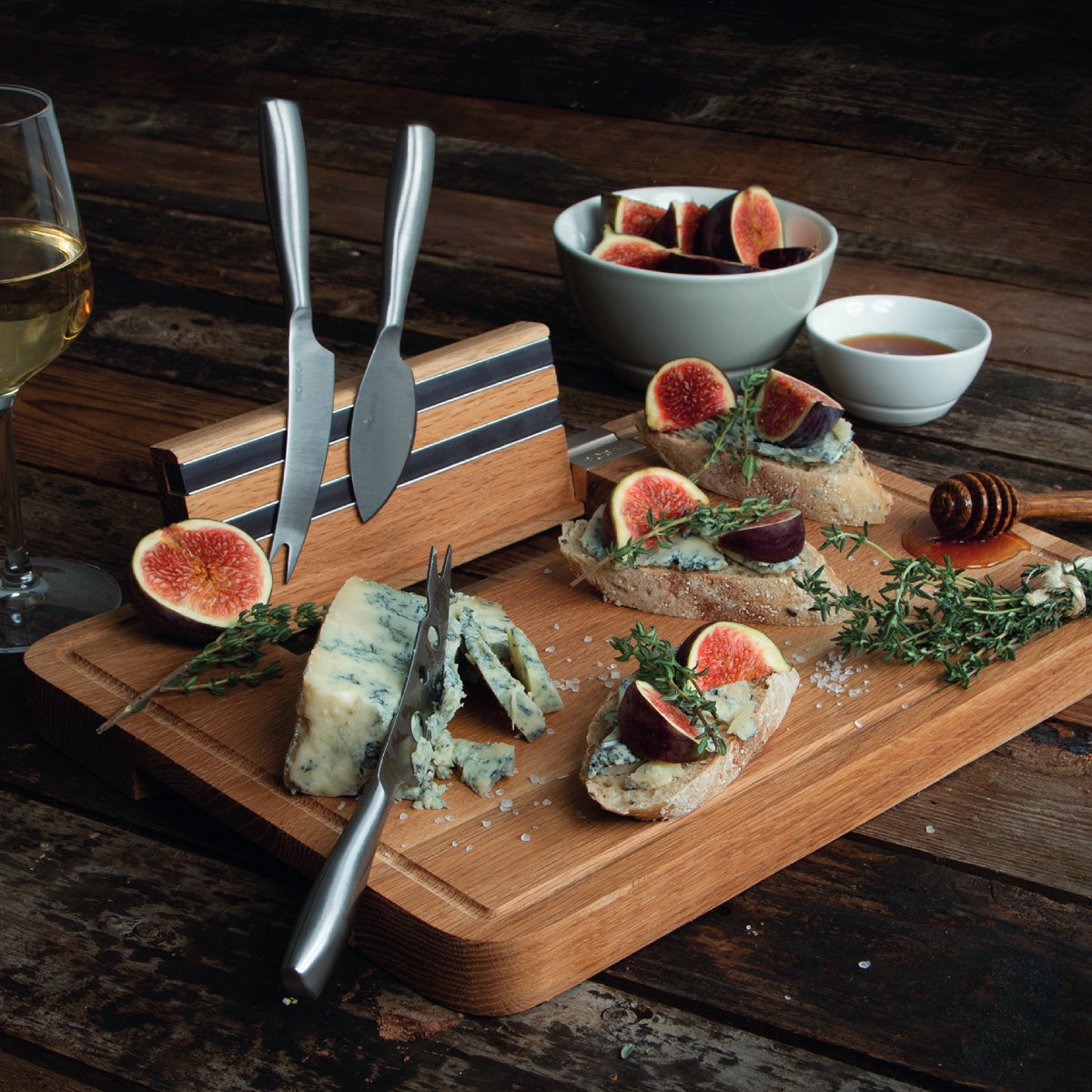 Wooden board with blue cheese, figs, crostini, honey, and wine glass.