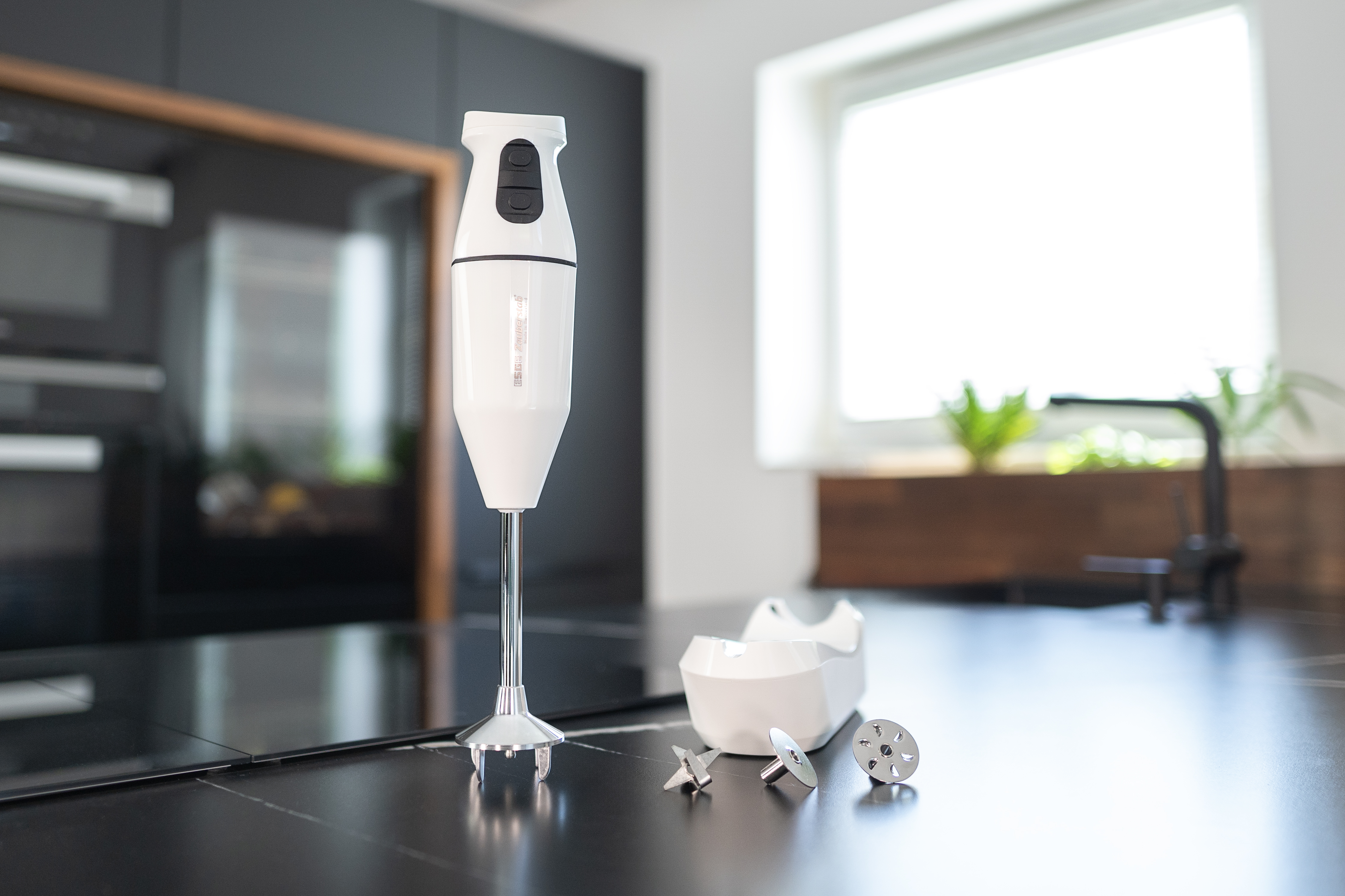 Biały blender ręczny z akcesoriami na czarnym blacie.