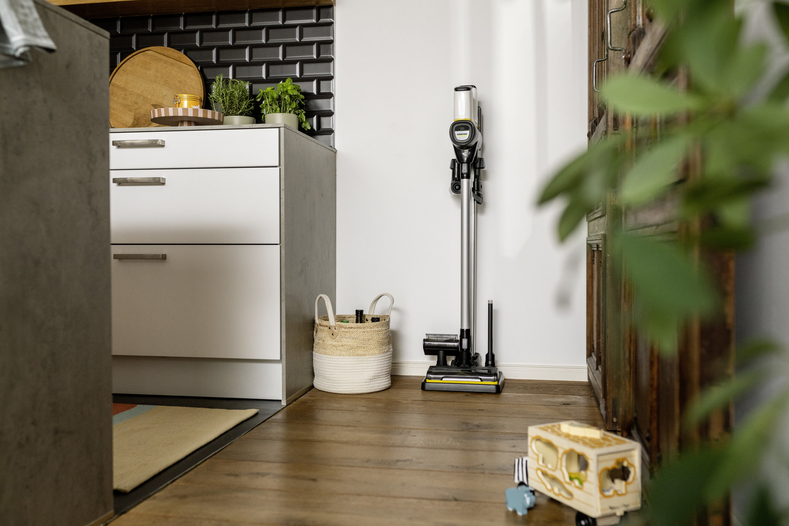 Un aspirateur moderne se dresse à côté d'un panier et d'une commode avec des plantes.
