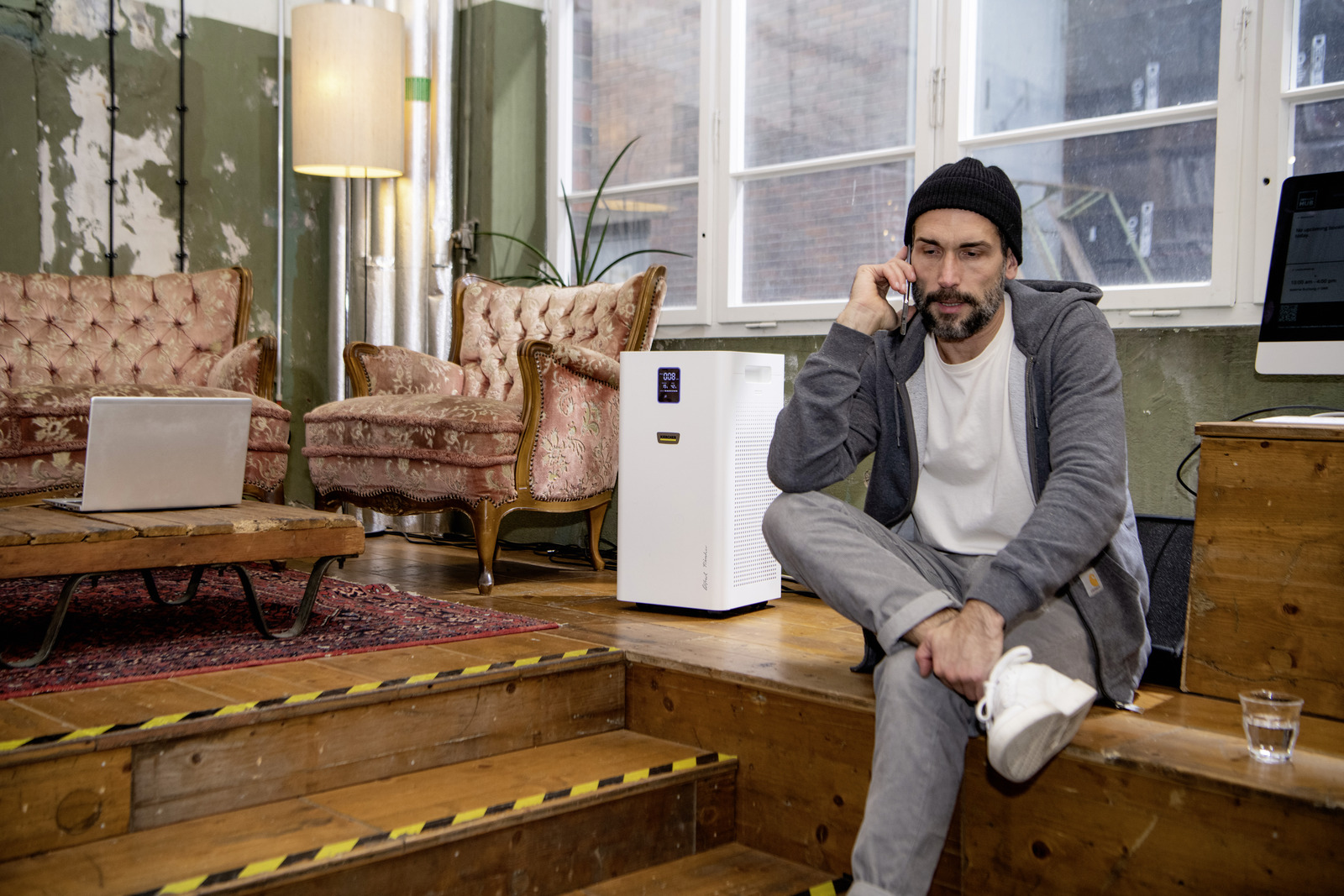 Man on phone by air purifier in rustic room with vintage furniture.