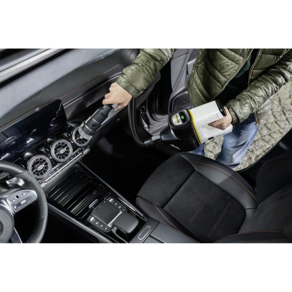 Personne nettoyant l'intérieur d'une voiture avec un aspirateur portable blanc et jaune.