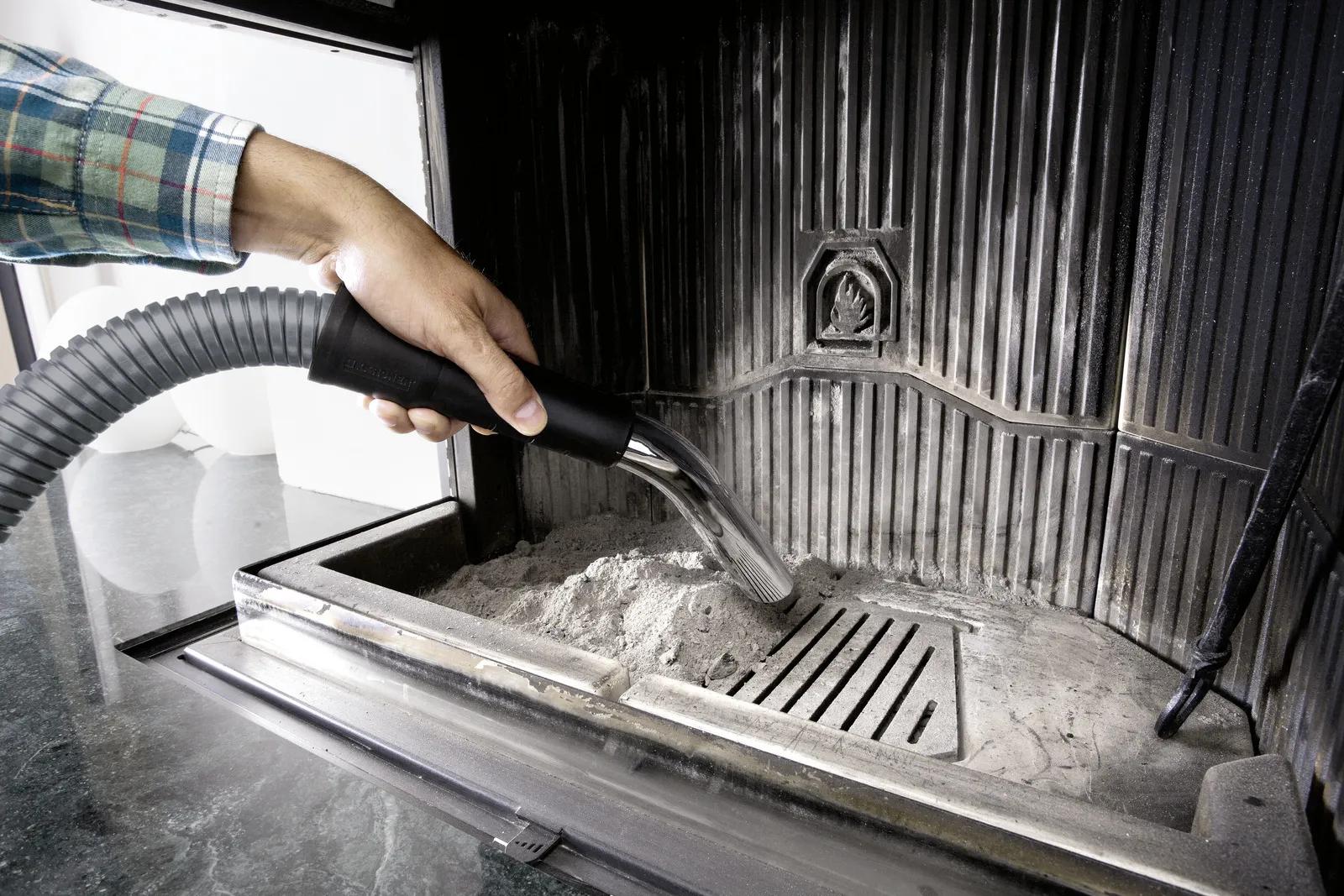 Ręka odkurza popiół z kominka za pomocą węża.