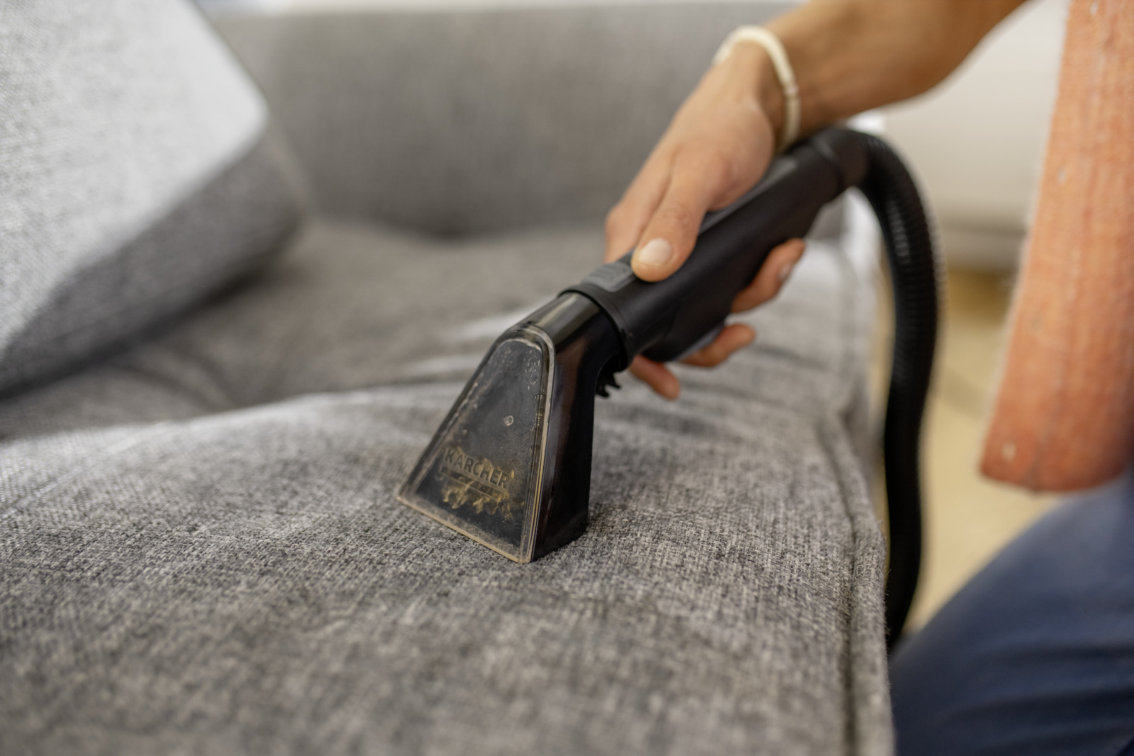 A hand uses a Karcher upholstery cleaner on a grey sofa.