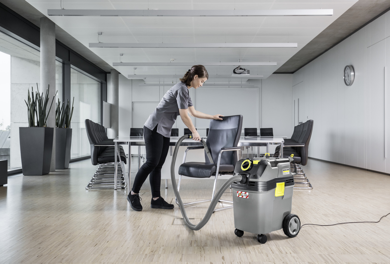 A woman vacuums a conference room chair with a Karcher vacuum cleaner.
