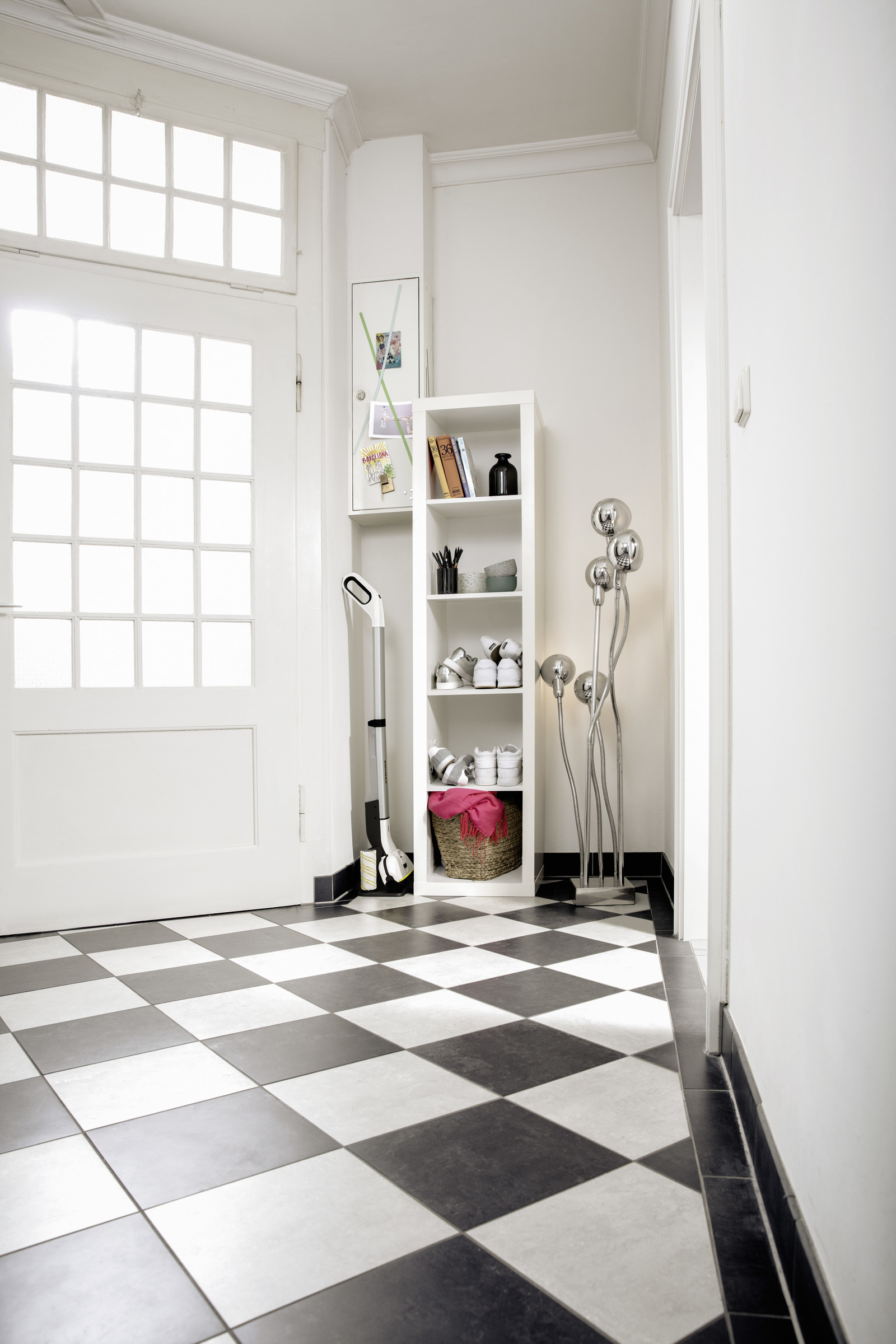 Przedpokój z kratowaną podłogą, białymi drzwiami i regałem.