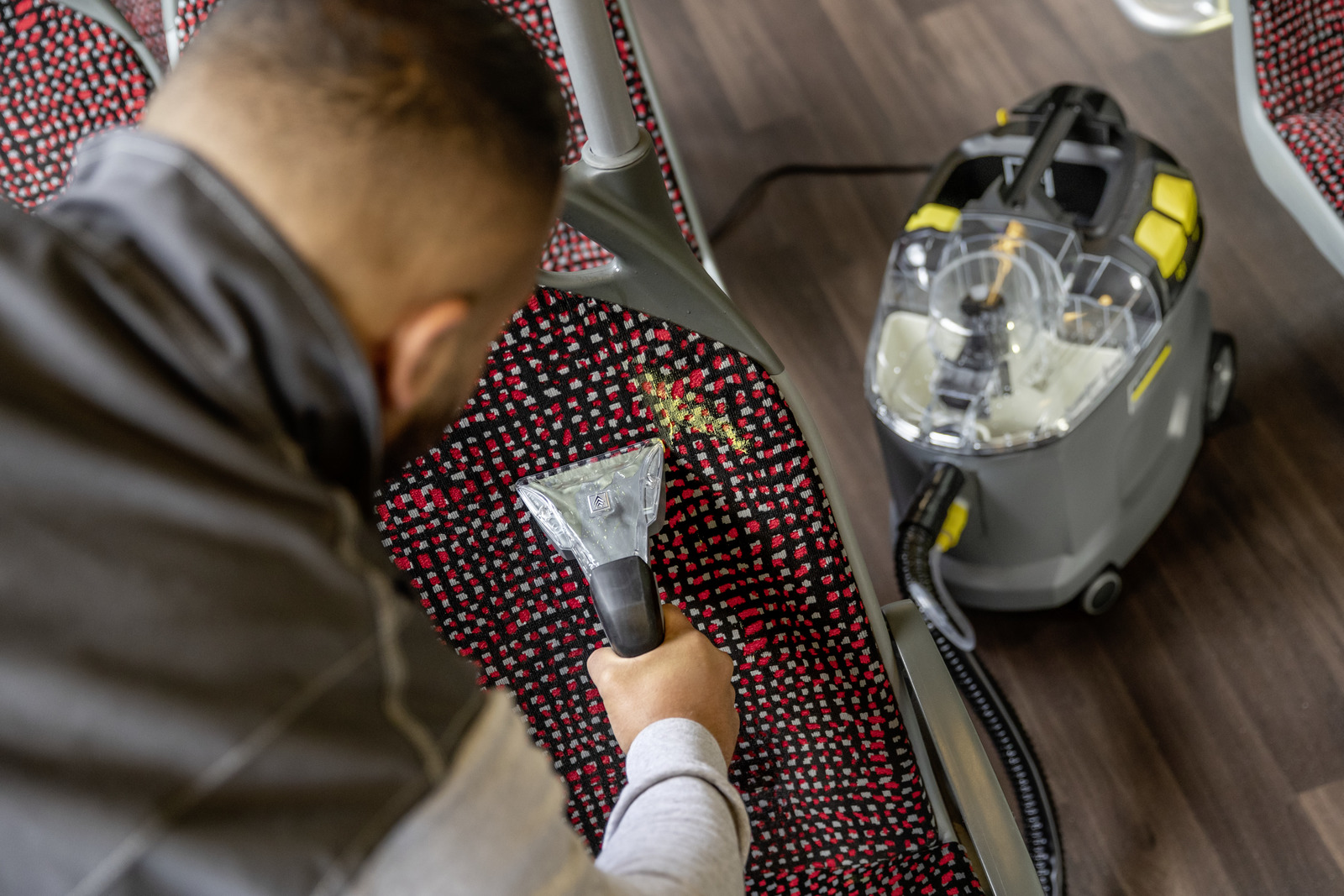 Mężczyzna czyści siedzenie ekstraktorem natryskowym i odkurzaczem.