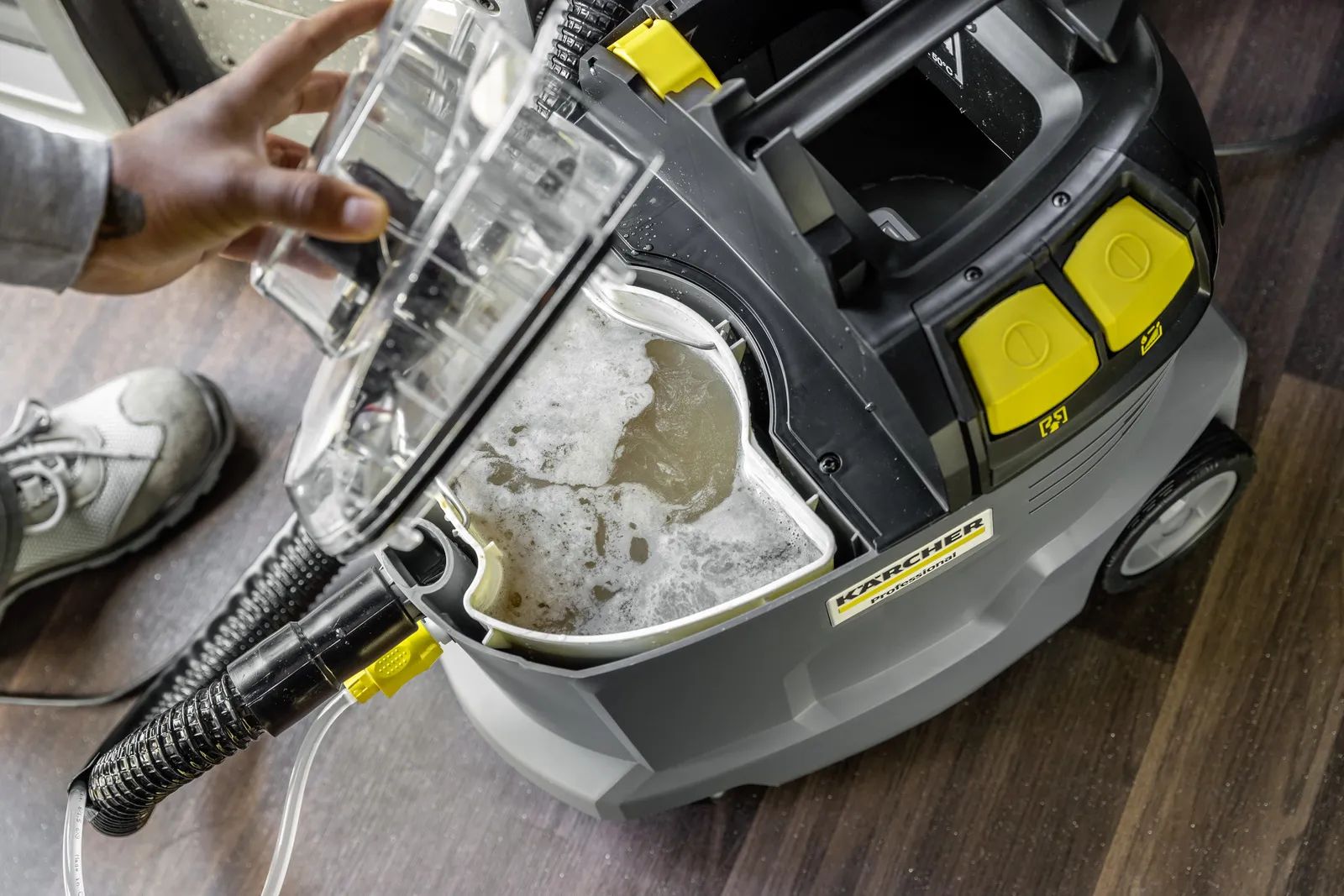 Ręka podnosi przezroczysty pojemnik z pieniącą się wodą z odkurzacza.