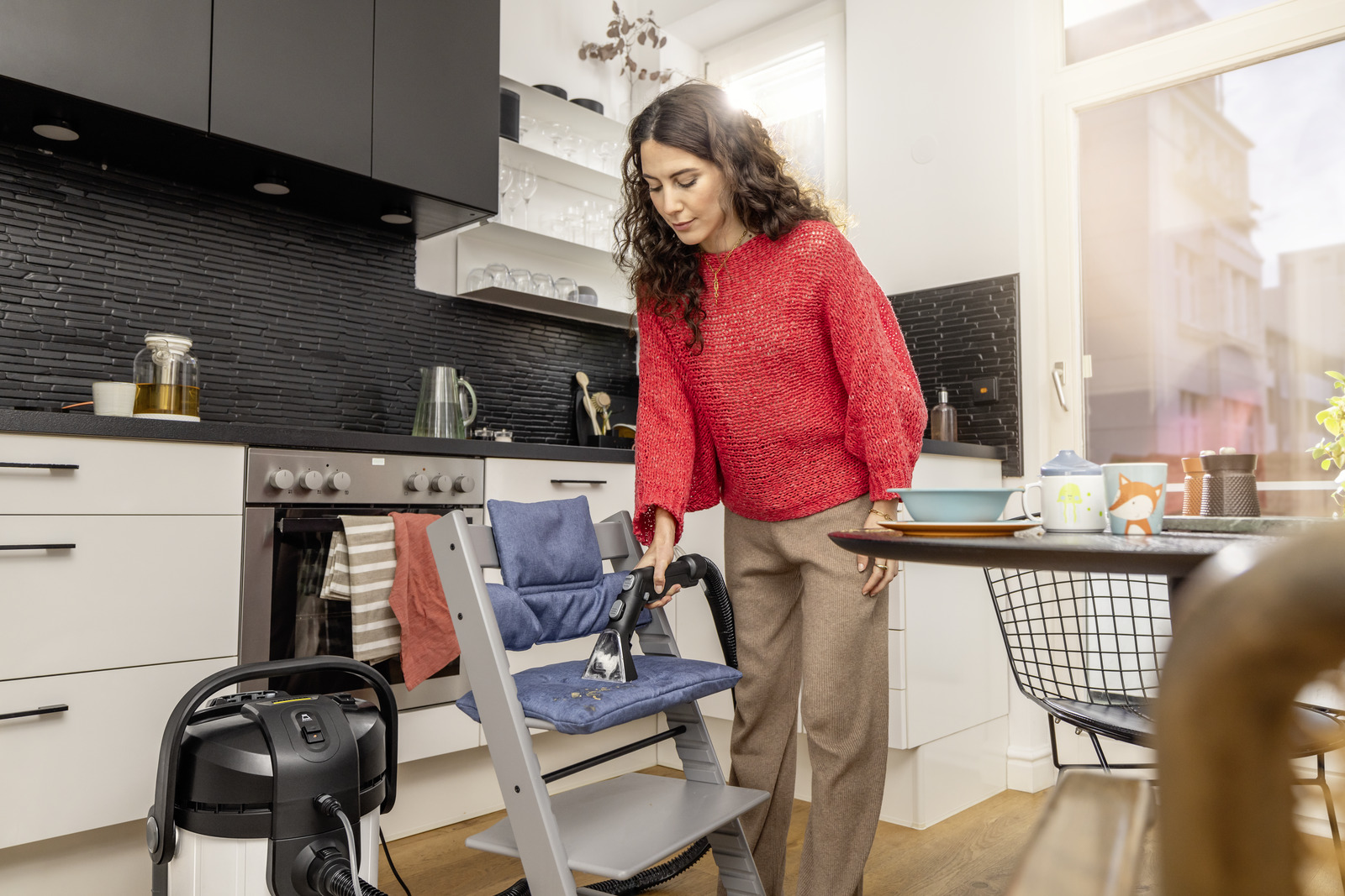 Kobieta czyści krzesełko do karmienia odkurzaczem na mokro/sucho w kuchni.
