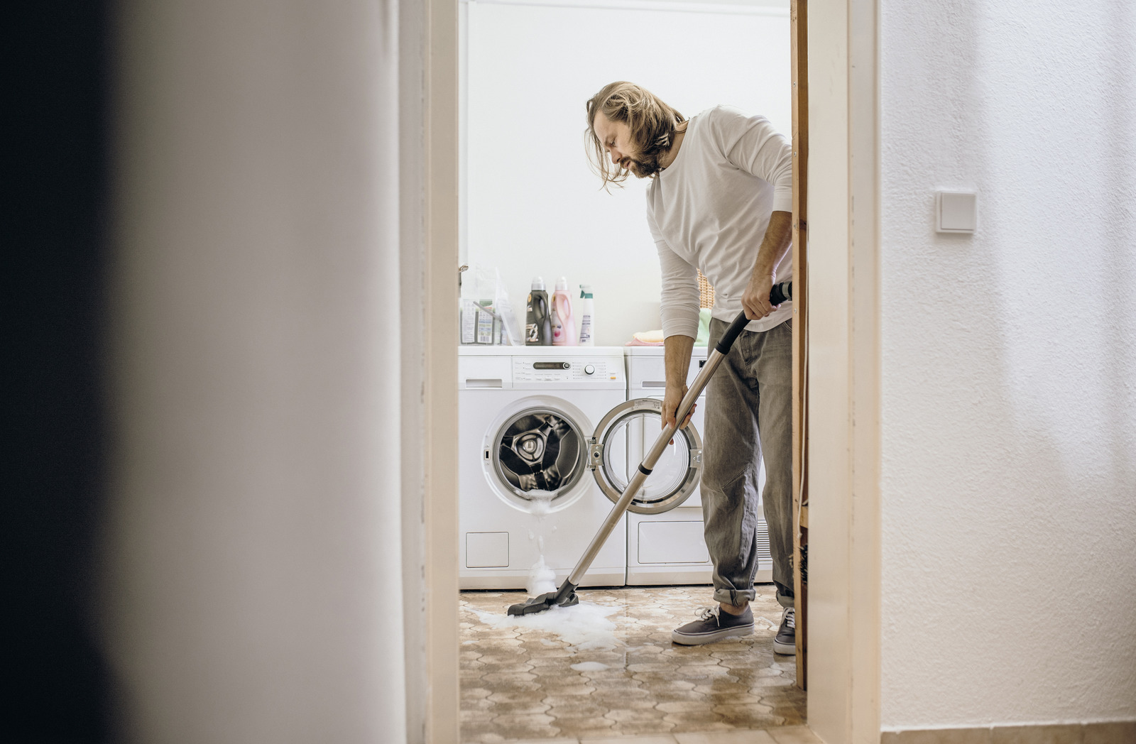 Mężczyzna odkurza rozlaną wodę przed pralkami odkurzaczem.