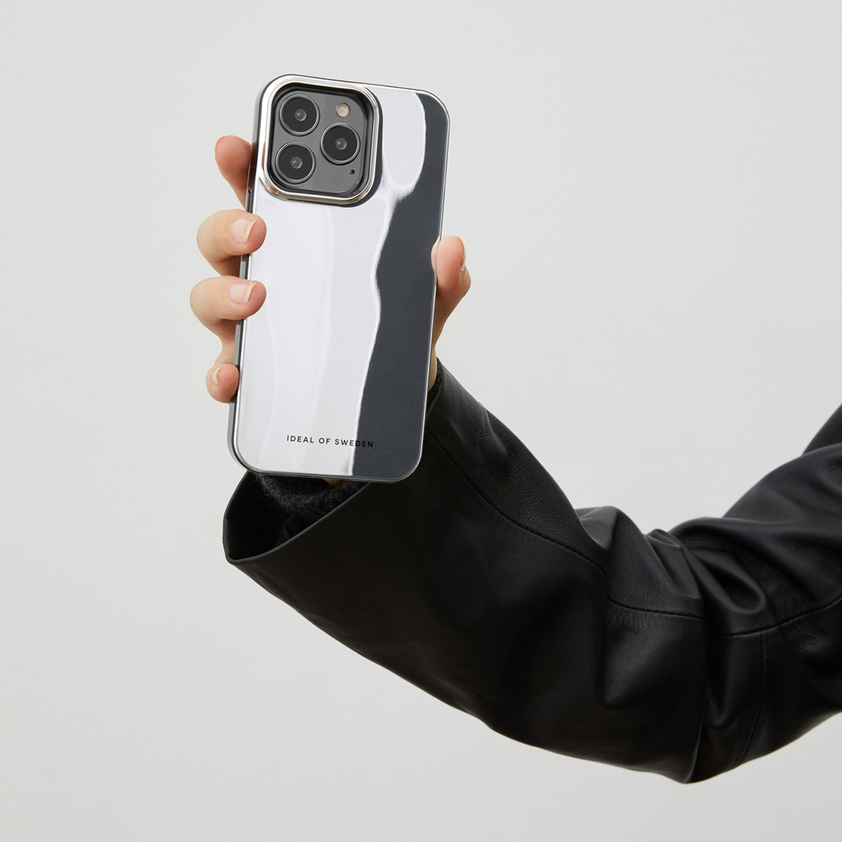 Eine Hand hält ein glänzendes, silbernes Handy mit drei Kameras.