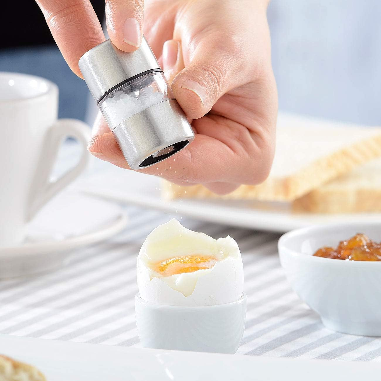 Salz wird über ein gekochtes Ei gestreut, daneben Toast und Marmelade.