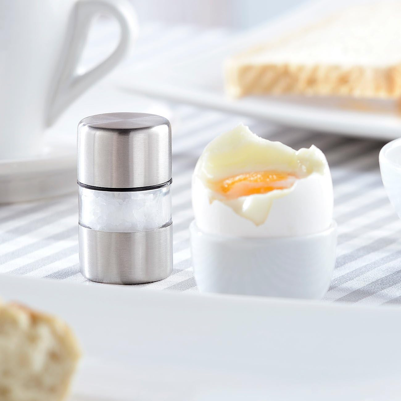 Ein weichgekochtes Ei im Becher neben einem Salzstreuer und Toast.
