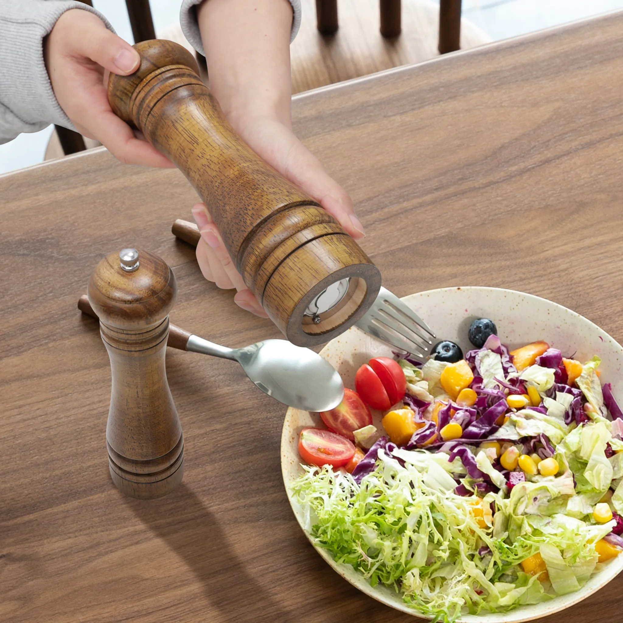 Holzmühle über Salat mit Tomaten, Beeren und Mais, wird von einer Hand gehalten.