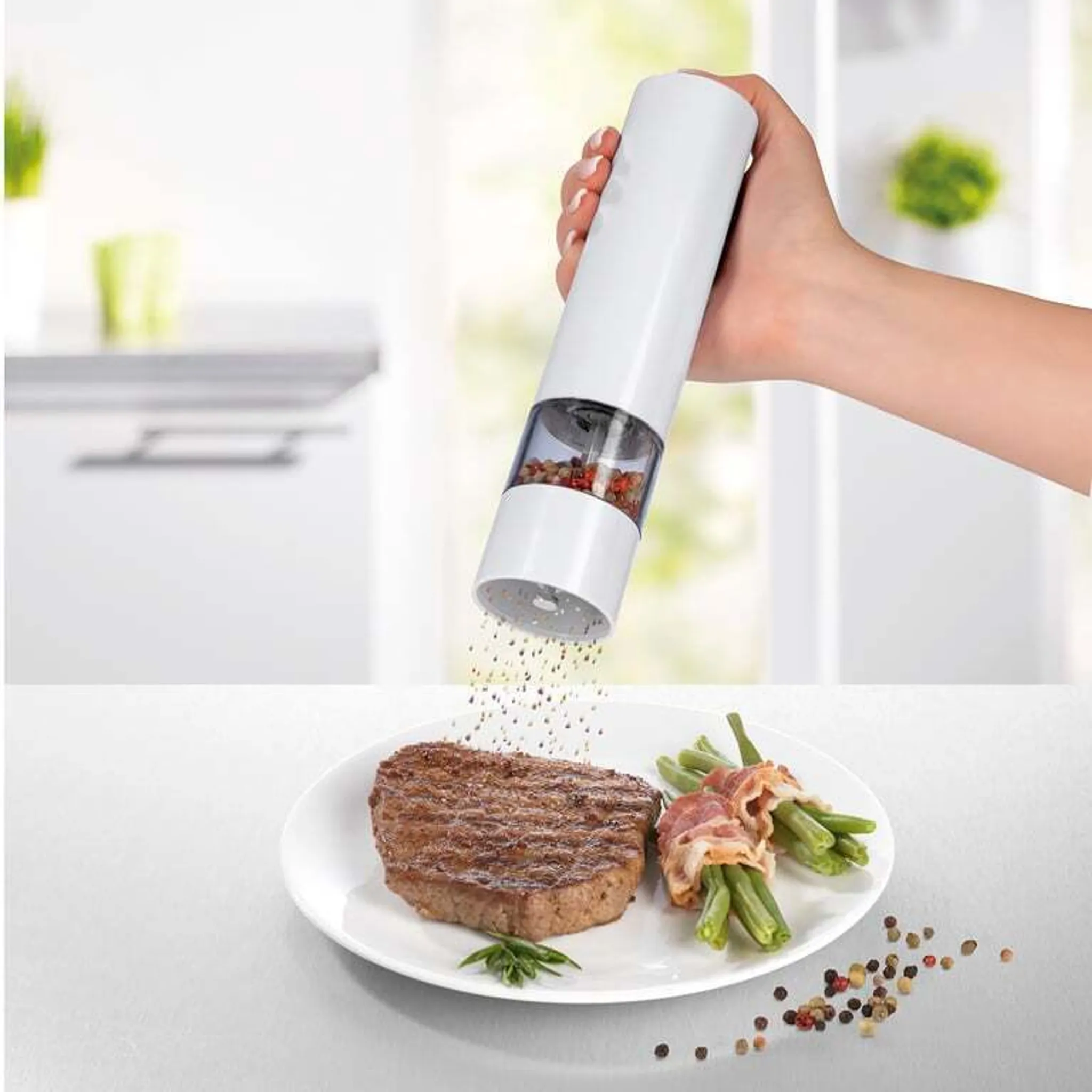 Eine Hand mahlt Pfeffer über ein Steak und grüne Bohnen mit Speck auf einem Teller.