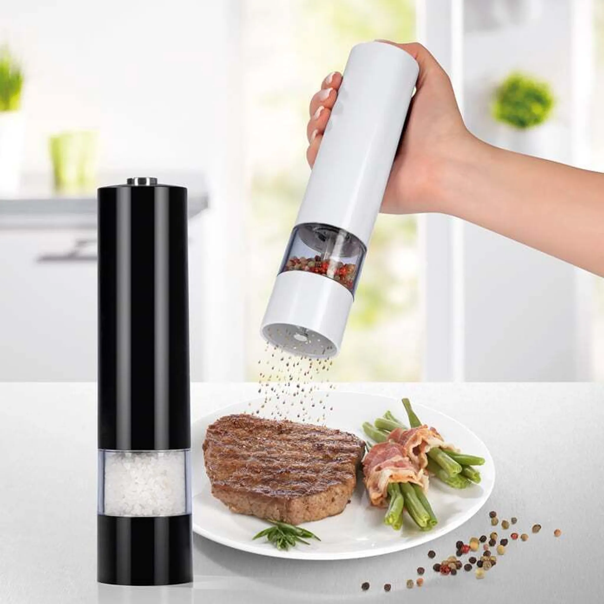 Elektrische Mühle mahlt Pfeffer über Steak und Speckbohnen auf einem Teller.
