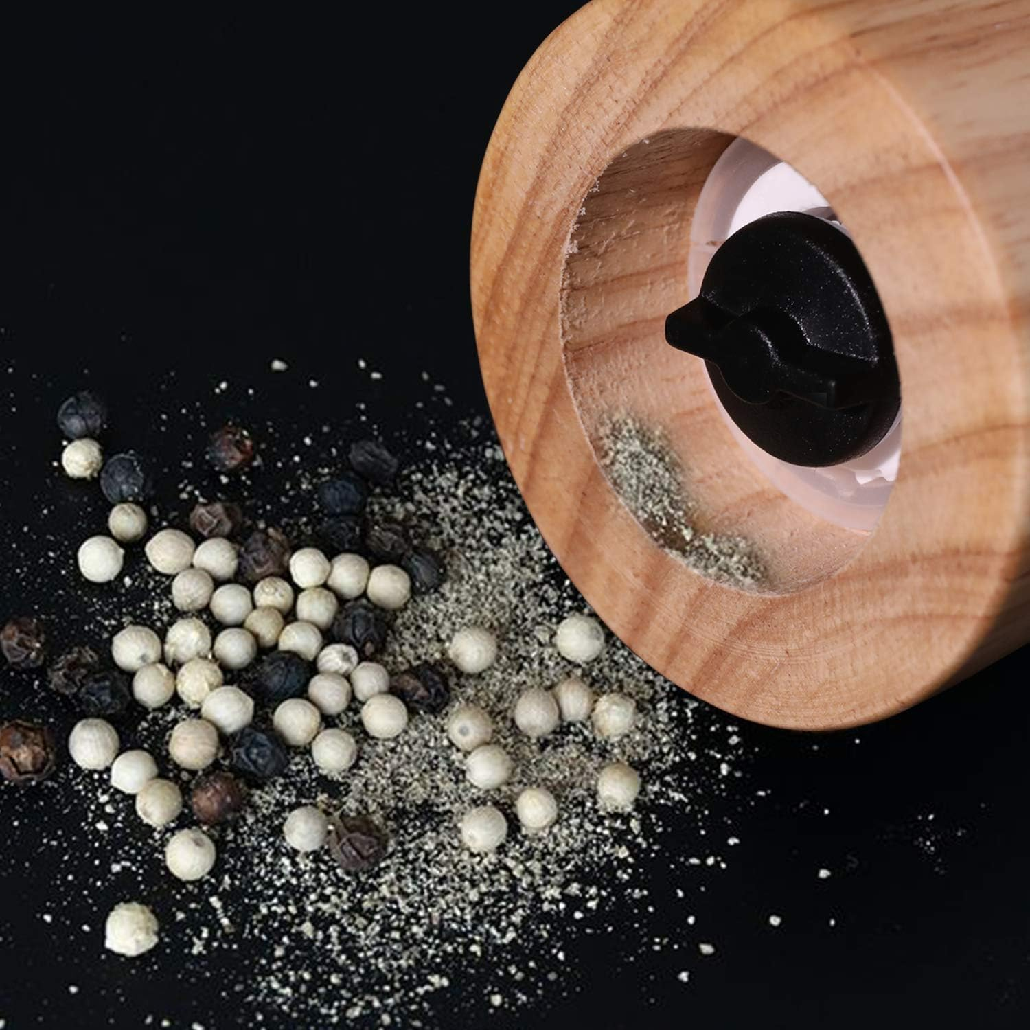 Holzmühle mit Pfefferkörnern und gemahlenem Pfeffer auf schwarzem Hintergrund.