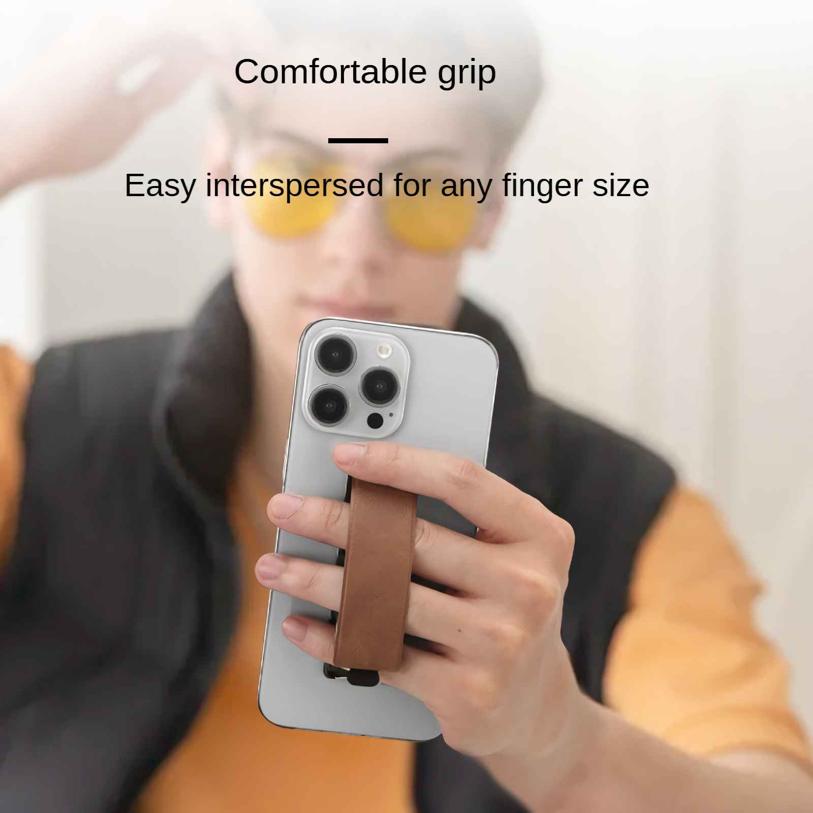 Eine Hand hält ein silbernes Smartphone mit einem braunen Griffband auf der Rückseite.
