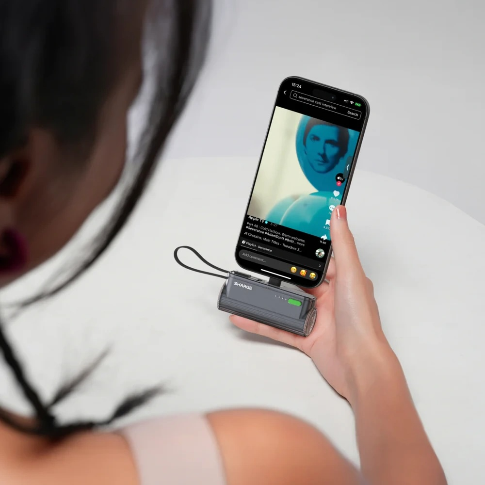 Une femme tient un smartphone soutenu par un chargeur portable. Une vidéo est affichée à l'écran.