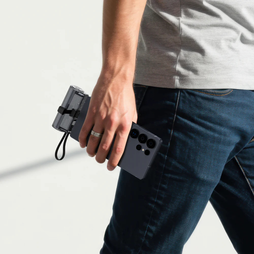 Homme tenant un smartphone sombre avec plusieurs caméras et une batterie transparente.