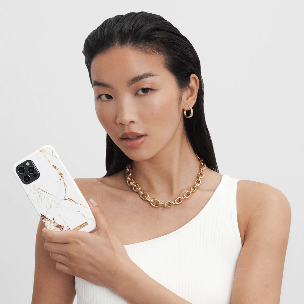 Una mujer de pelo oscuro sostiene un teléfono blanco con diseño de mármol.