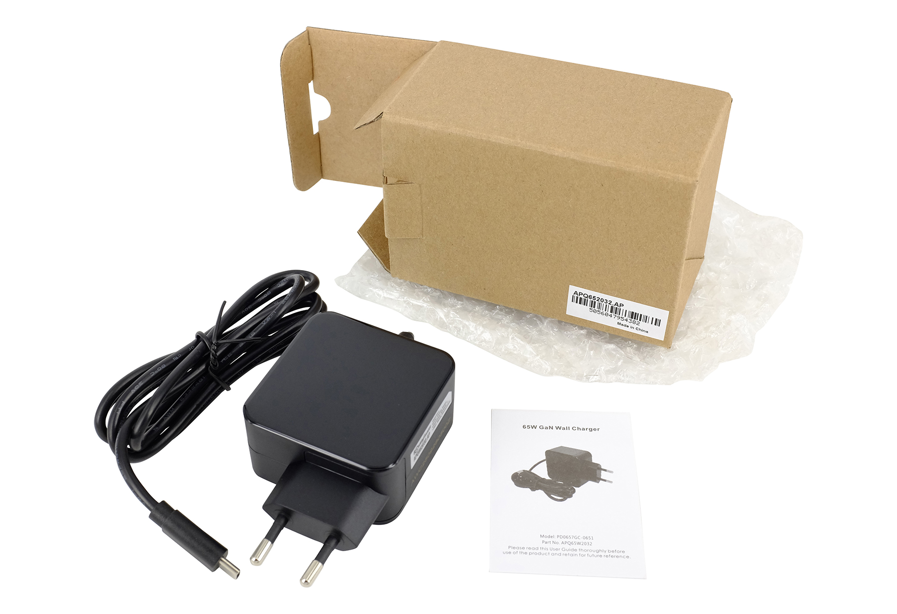 Ein schwarzes Netzteil, Kabel und Handbuch liegen neben einer offenen Pappschachtel.