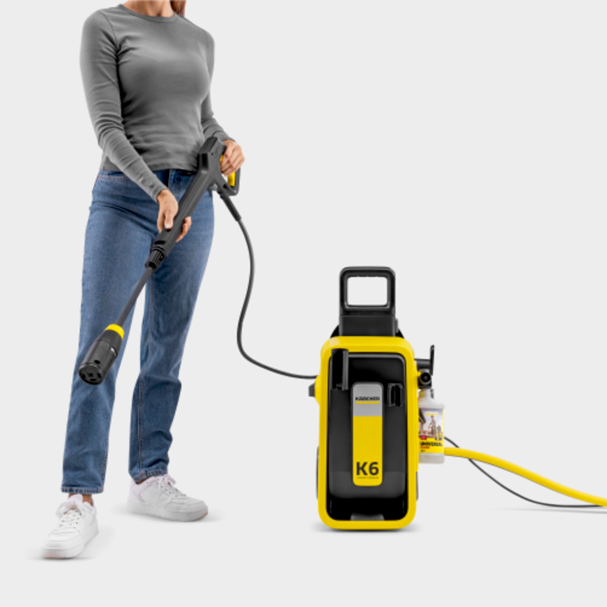 Una donna in jeans tiene un'idropulitrice. Accanto a lei c'è un dispositivo giallo.