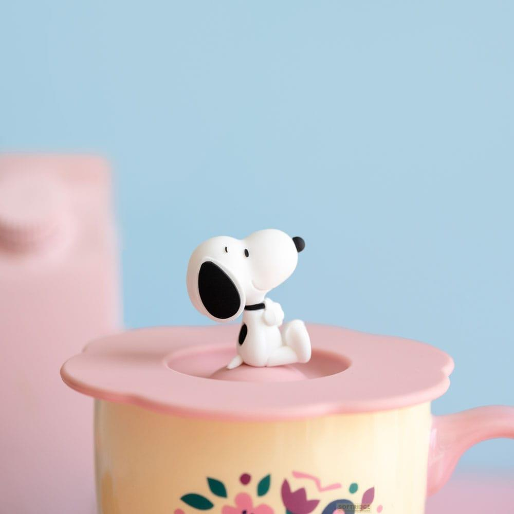 Snoopy-Figur sitzt auf einem gelben Becher mit Blumenmuster und rosafarbenem Deckel.
