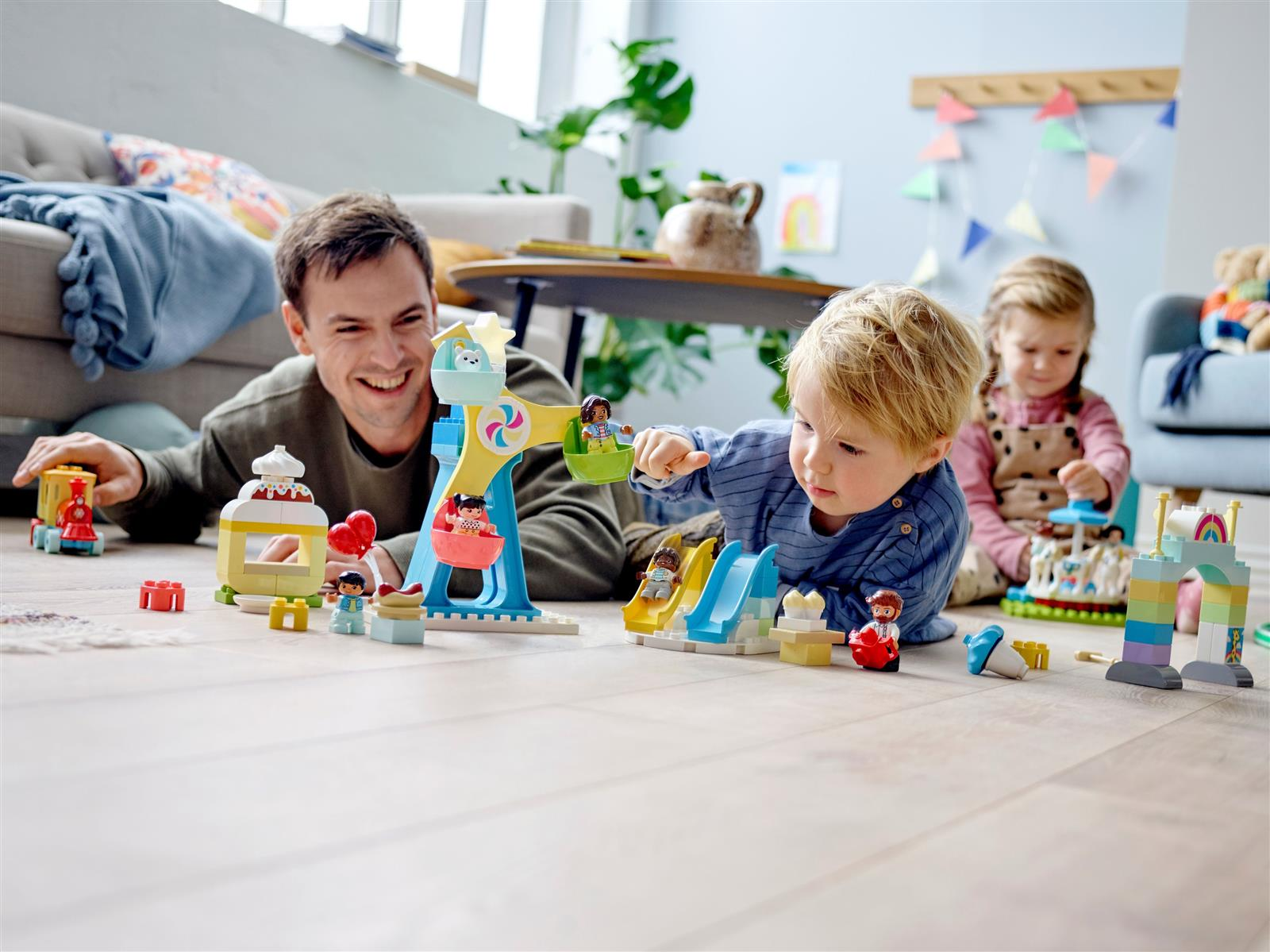Vater und Kinder spielen mit bunten Duplo-Spielzeugen auf dem Boden.