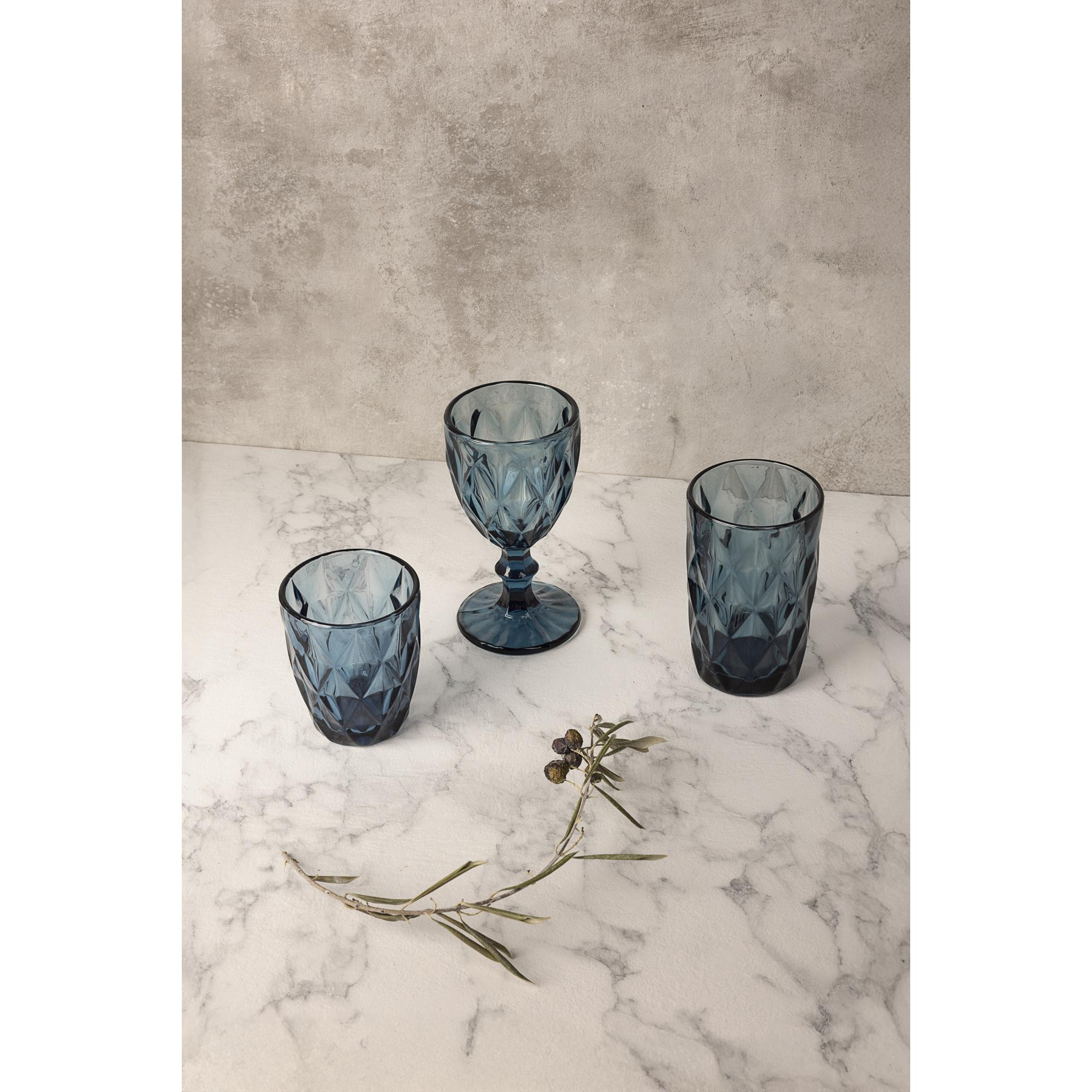 Tres vasos azules de rombos sobre mármol, con una ramita de bayas.