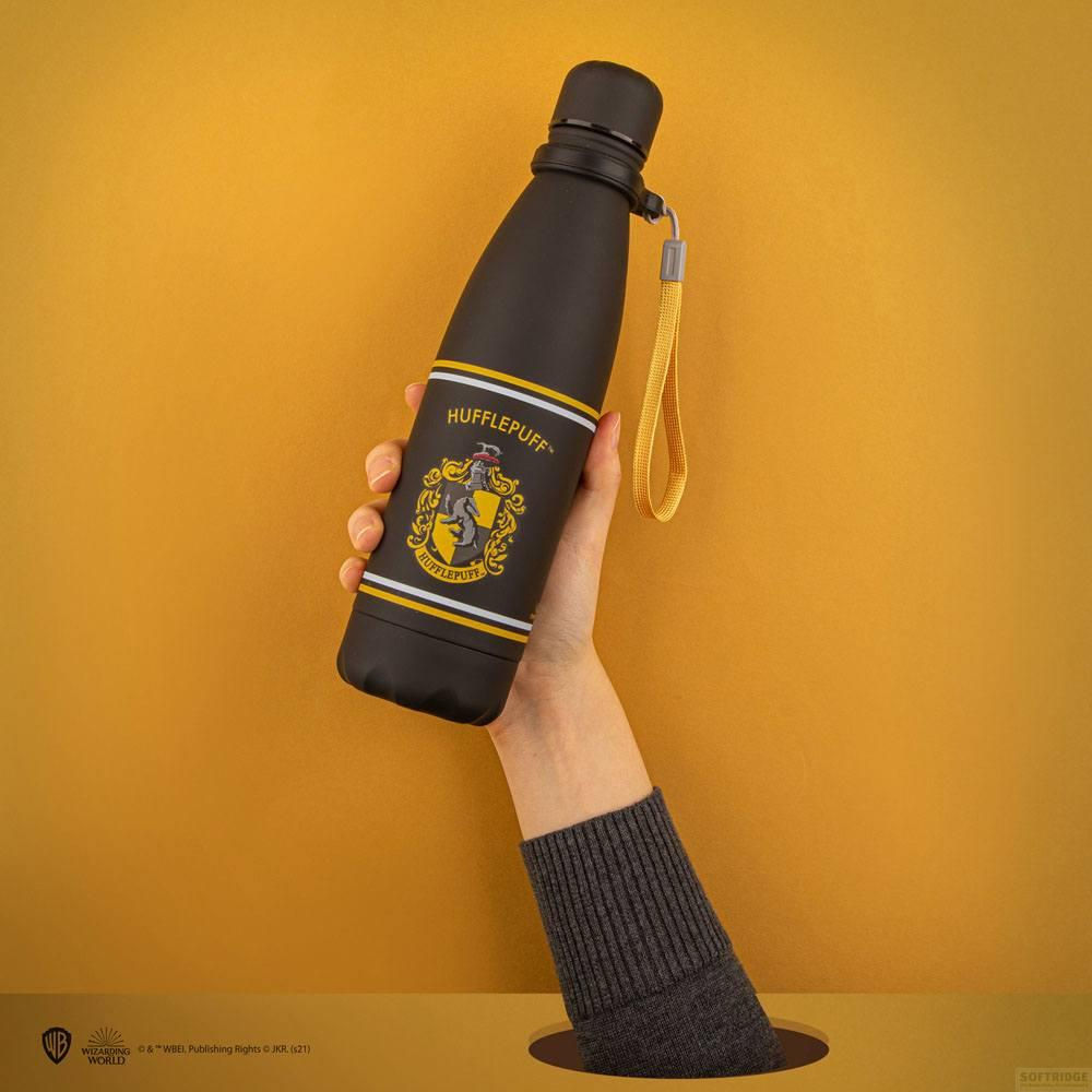Schwarze Hufflepuff-Flasche mit gelbem Band, gehalten von einer Hand, vor gelbem Hintergrund.