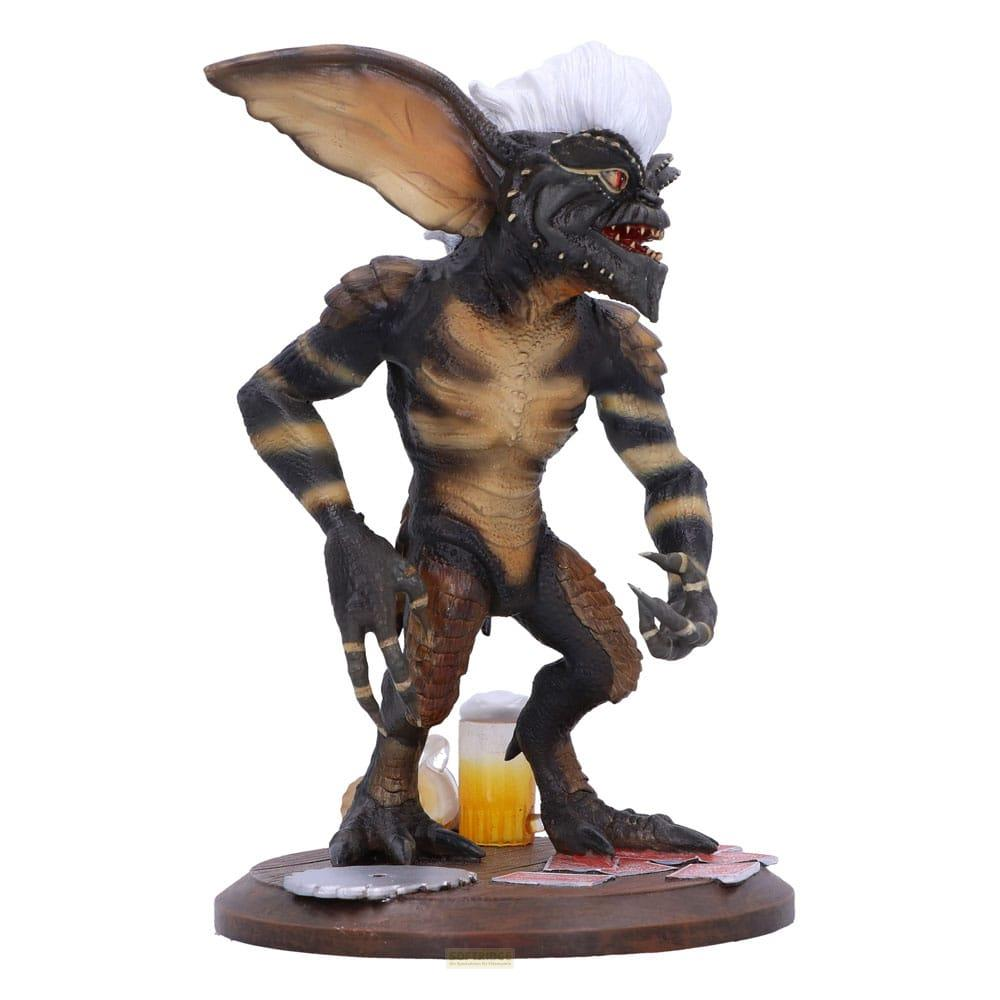 Eine Gremlin-Figur mit weißem Haar steht neben einem Bierkrug auf einem Holzteller.