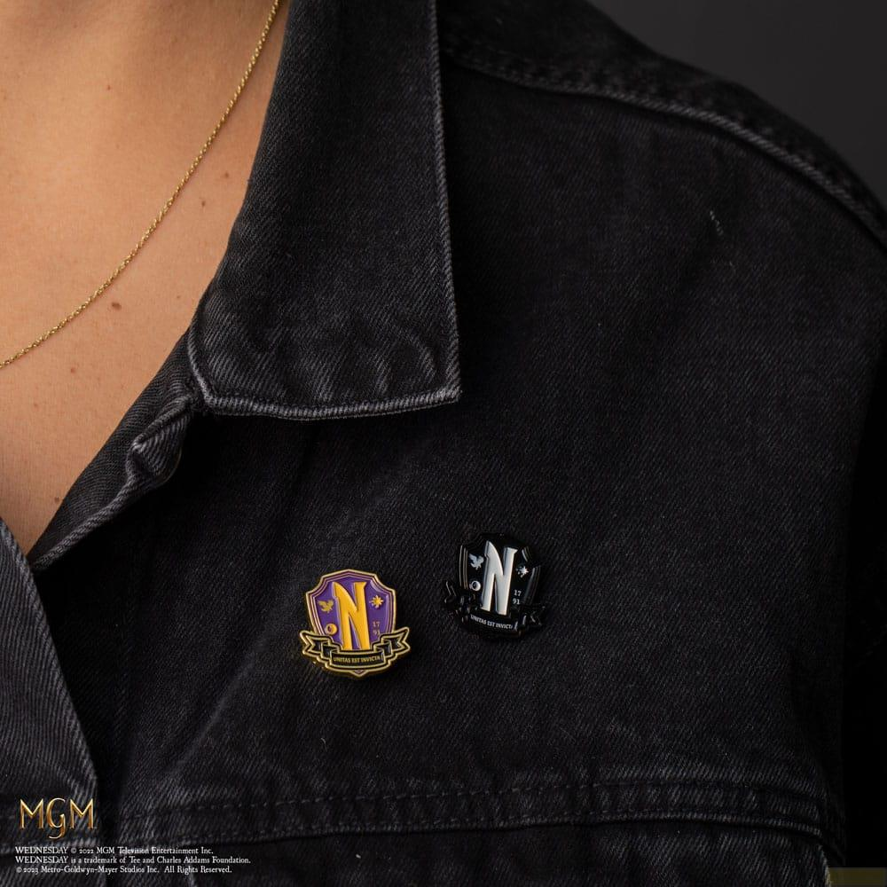 Dos pines de escudo escolar en una chaqueta vaquera negra: morado con 'N' dorada, negro con 'N' blanca.