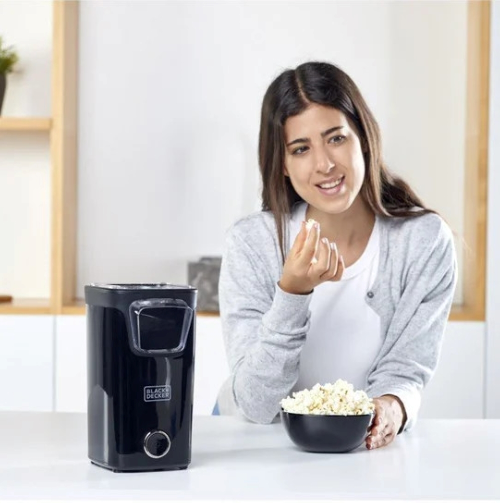 Donna mangia popcorn accanto a una macchina per popcorn nera.