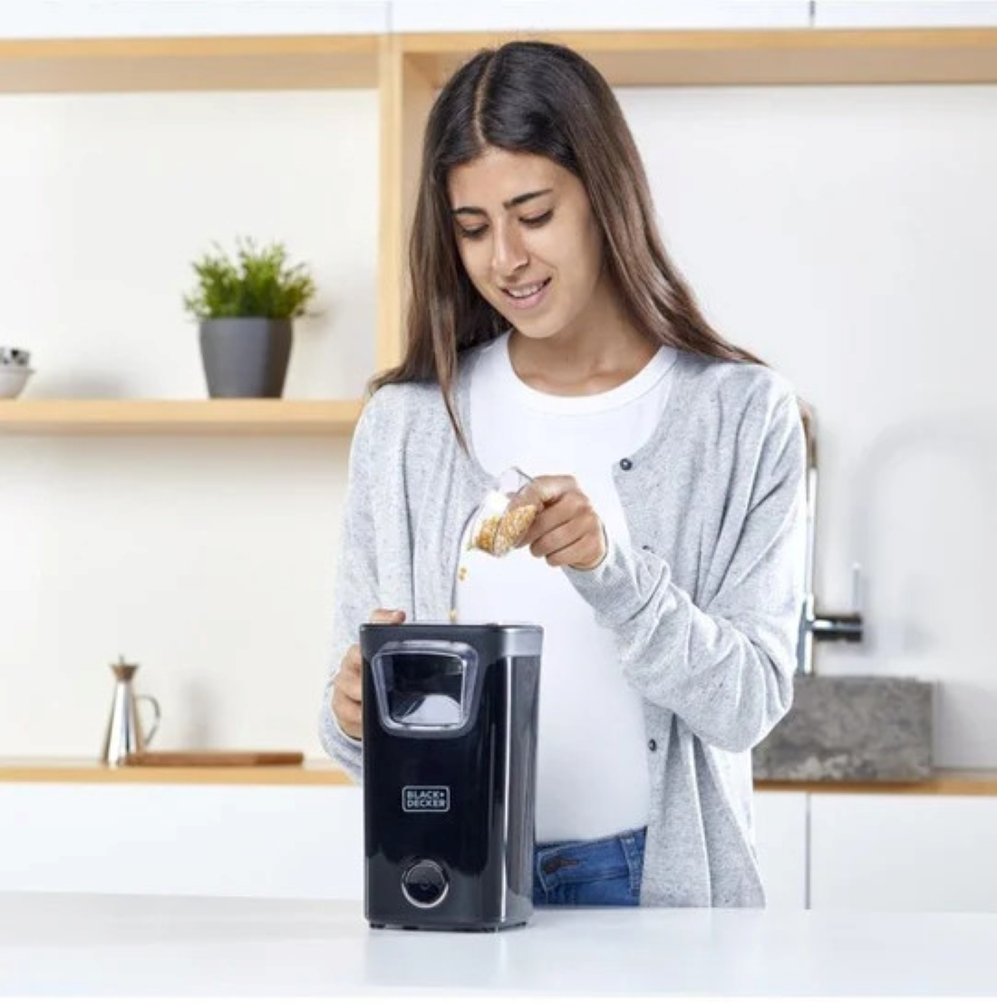Una donna versa chicchi in un elettrodomestico da cucina nero su un piano di lavoro bianco.