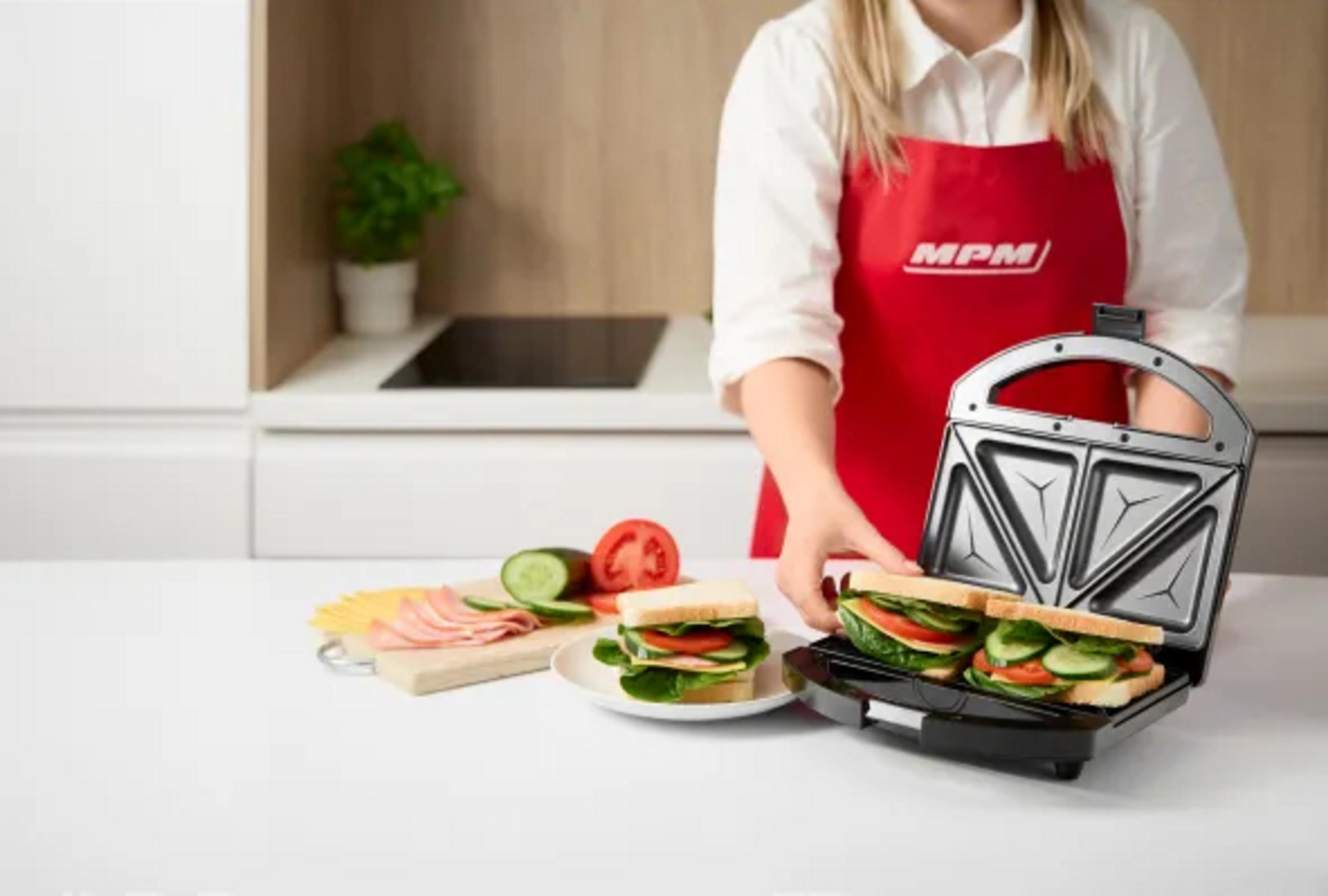 Una donna con grembiule rosso prepara panini in un tostapane.