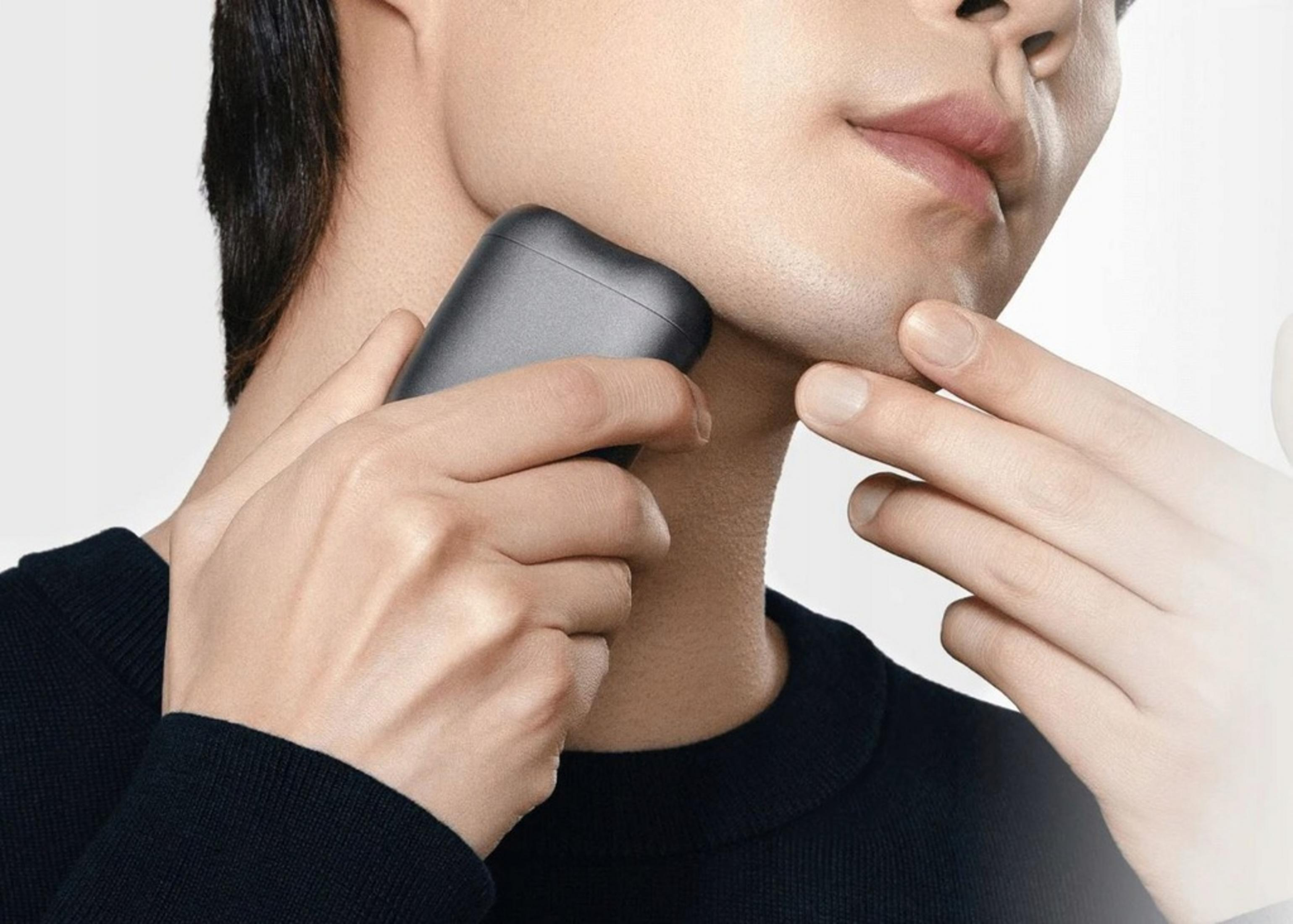 Mężczyzna goli podbródek i szyję małą, ciemną golarką elektryczną.