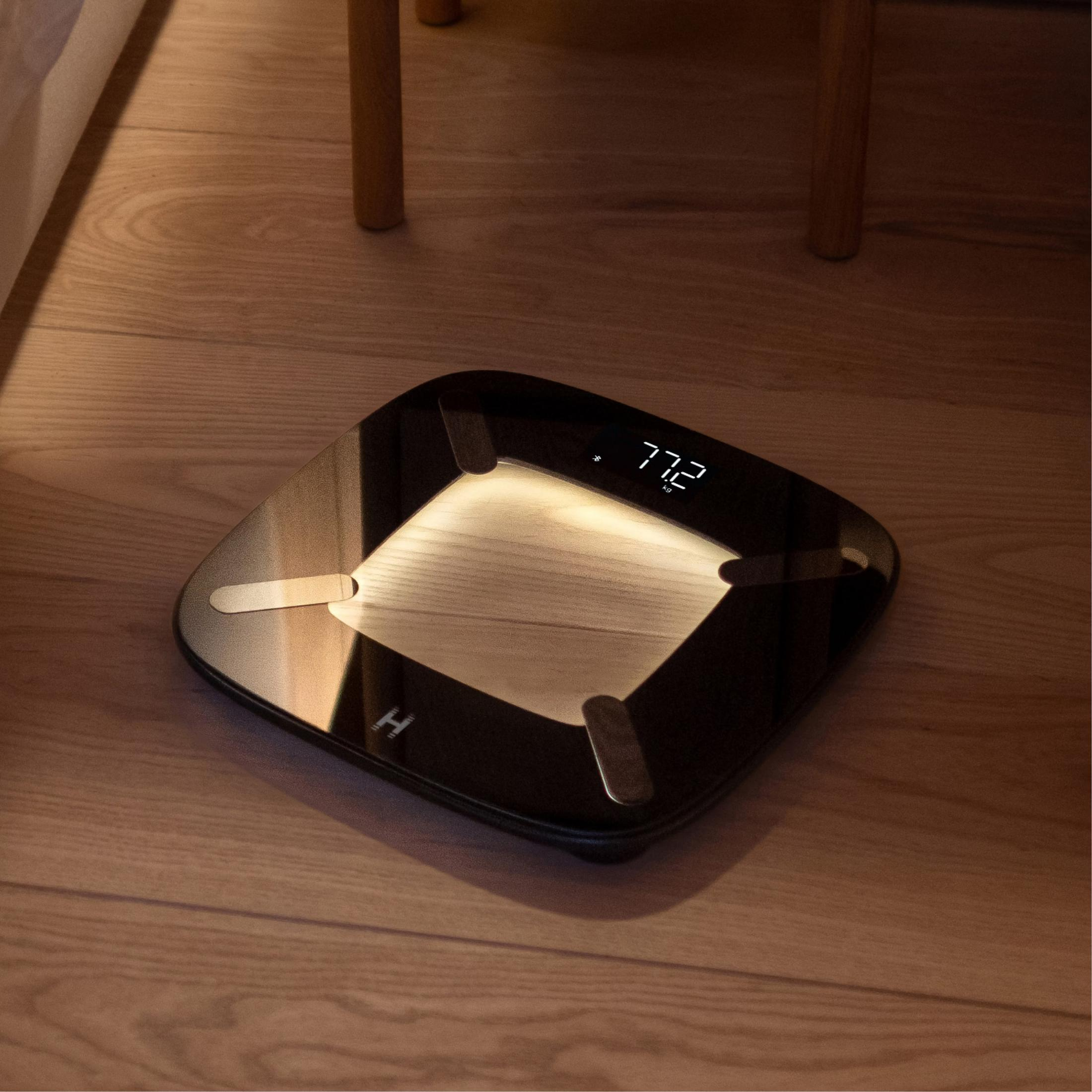 Czarna cyfrowa waga z drewnianym detalem pokazuje 77,2 kg.