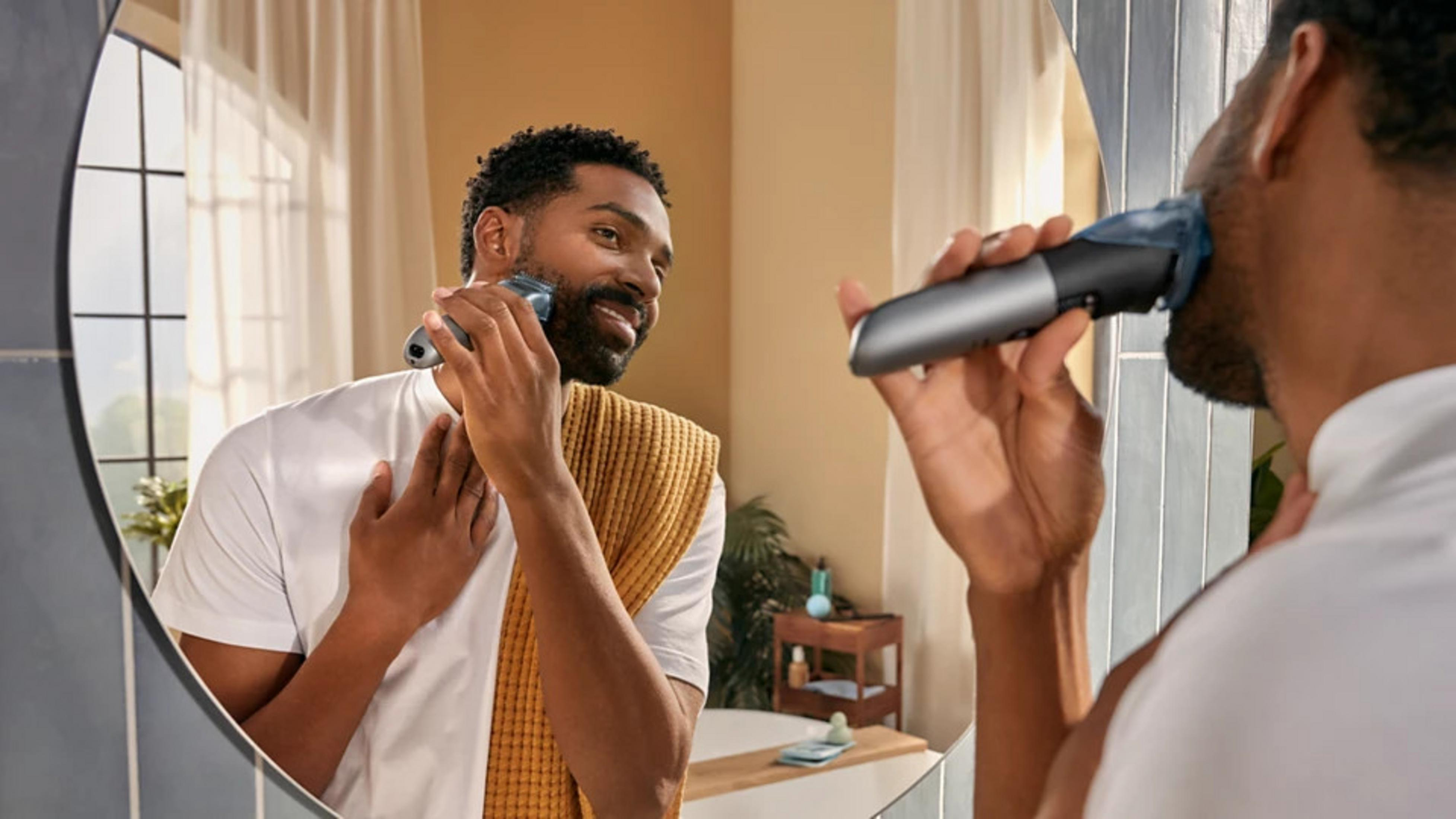 Un uomo si rade la barba allo specchio con un rasoio elettrico.