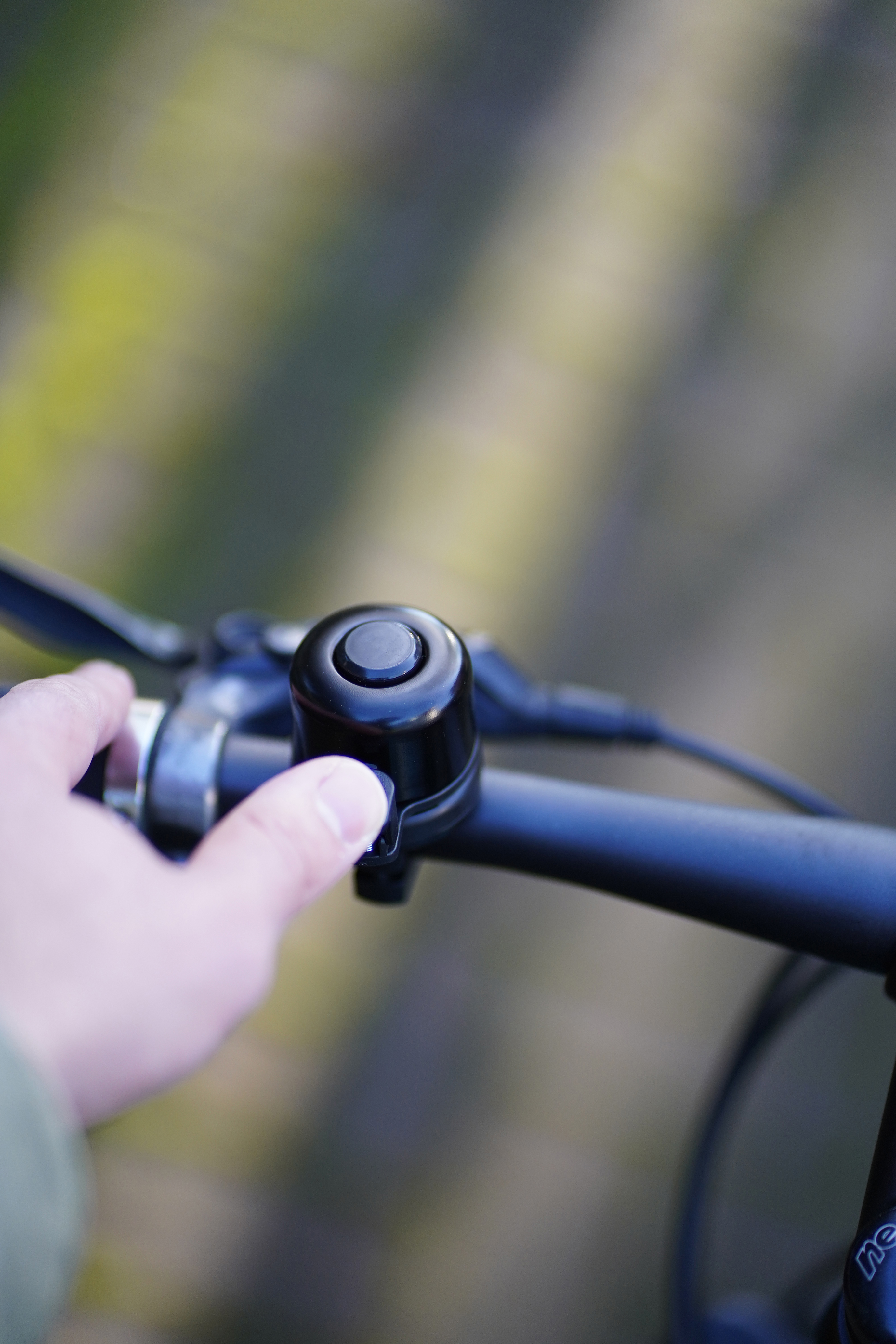Eine Hand drückt eine schwarze Fahrradklingel auf einem Lenker.