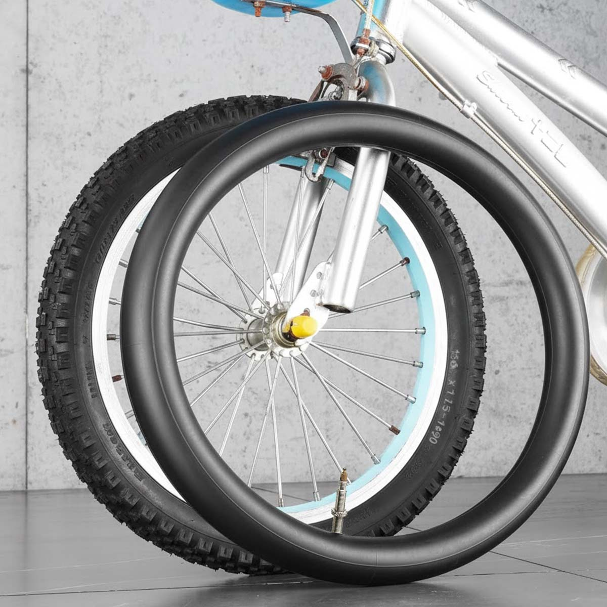 Ein Fahrradschlauch liegt vor einem Fahrradreifen auf Beton.