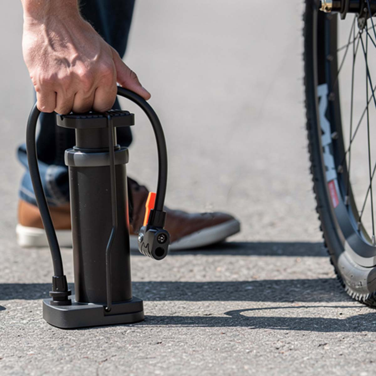 Person pumpt Fahrradreifen mit schwarzer Pumpe auf einem asphaltierten Weg auf.