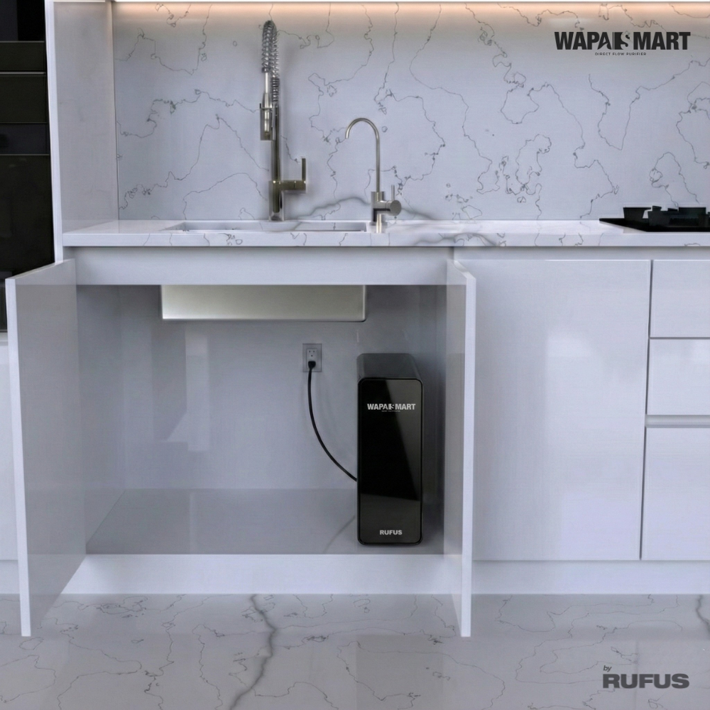 Un purificador de agua negro est&aacute; debajo de un fregadero de cocina con grifo plateado y encimera de m&aacute;rmol.
