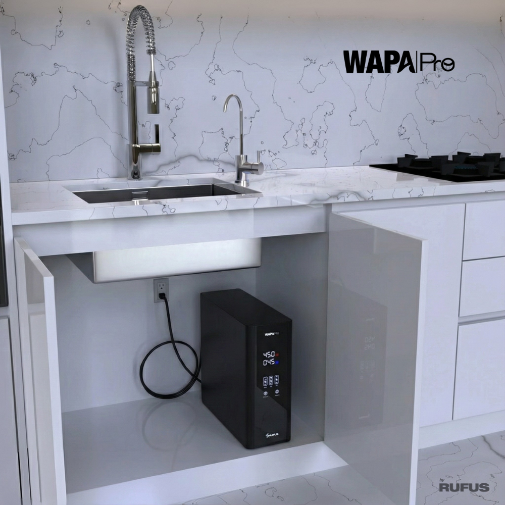 Un filtro de agua negro está debajo de un fregadero junto a un cable de alimentación.